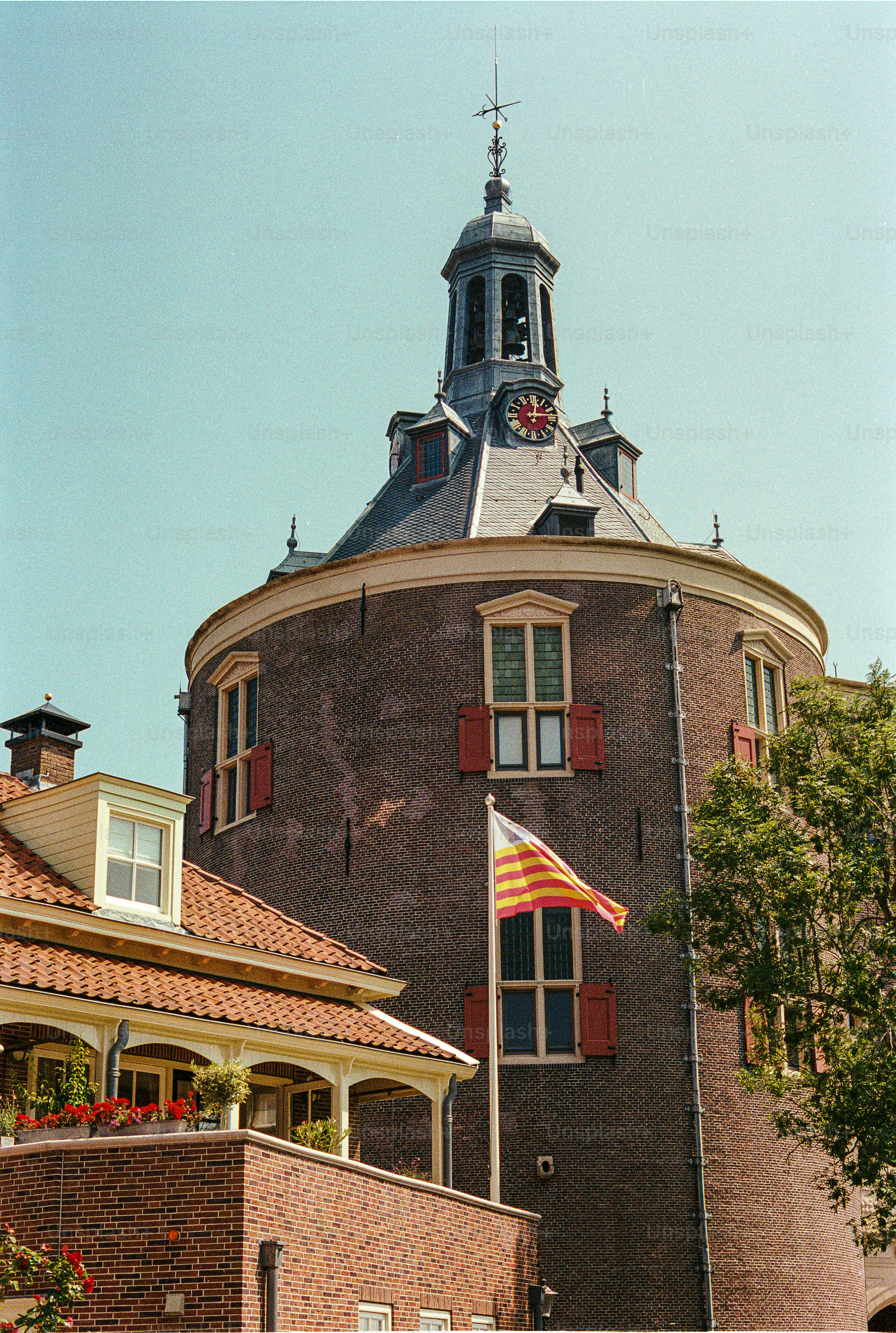 Edificio redondo de ladrillo con una torre del reloj y una bandera.