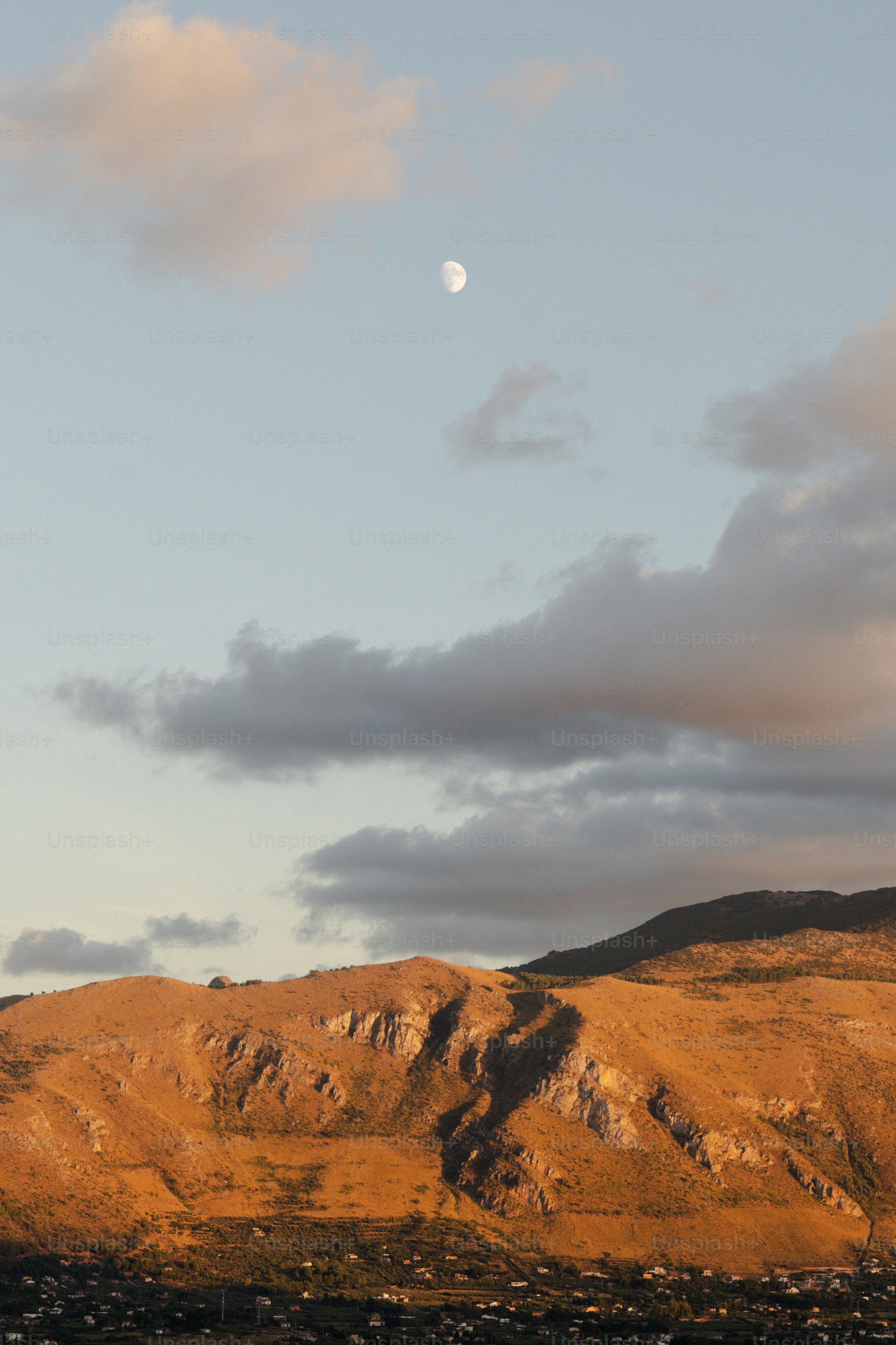 Moon visible in sky over golden hills at sunset