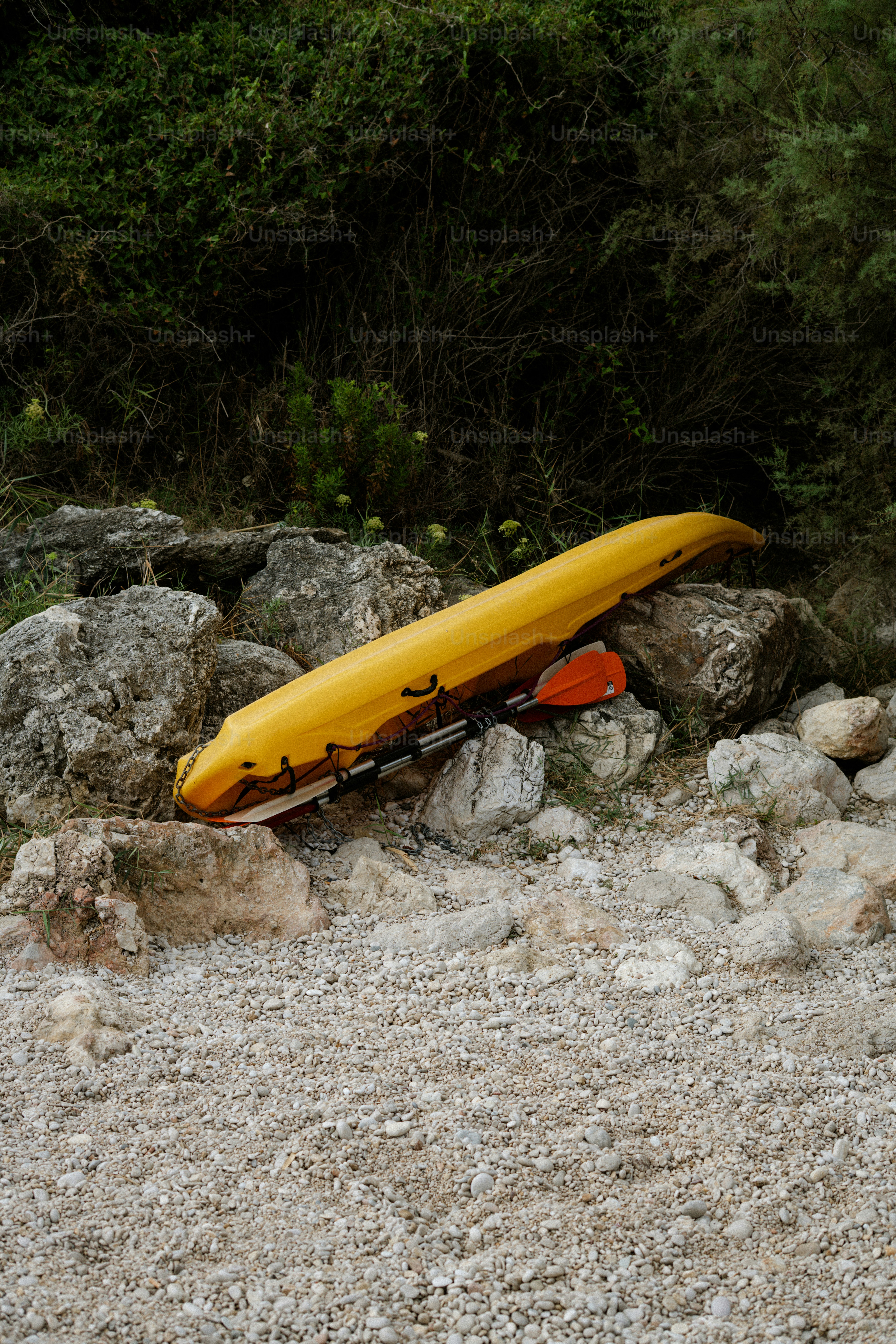 A yellow kayak rests on a rocky shore.