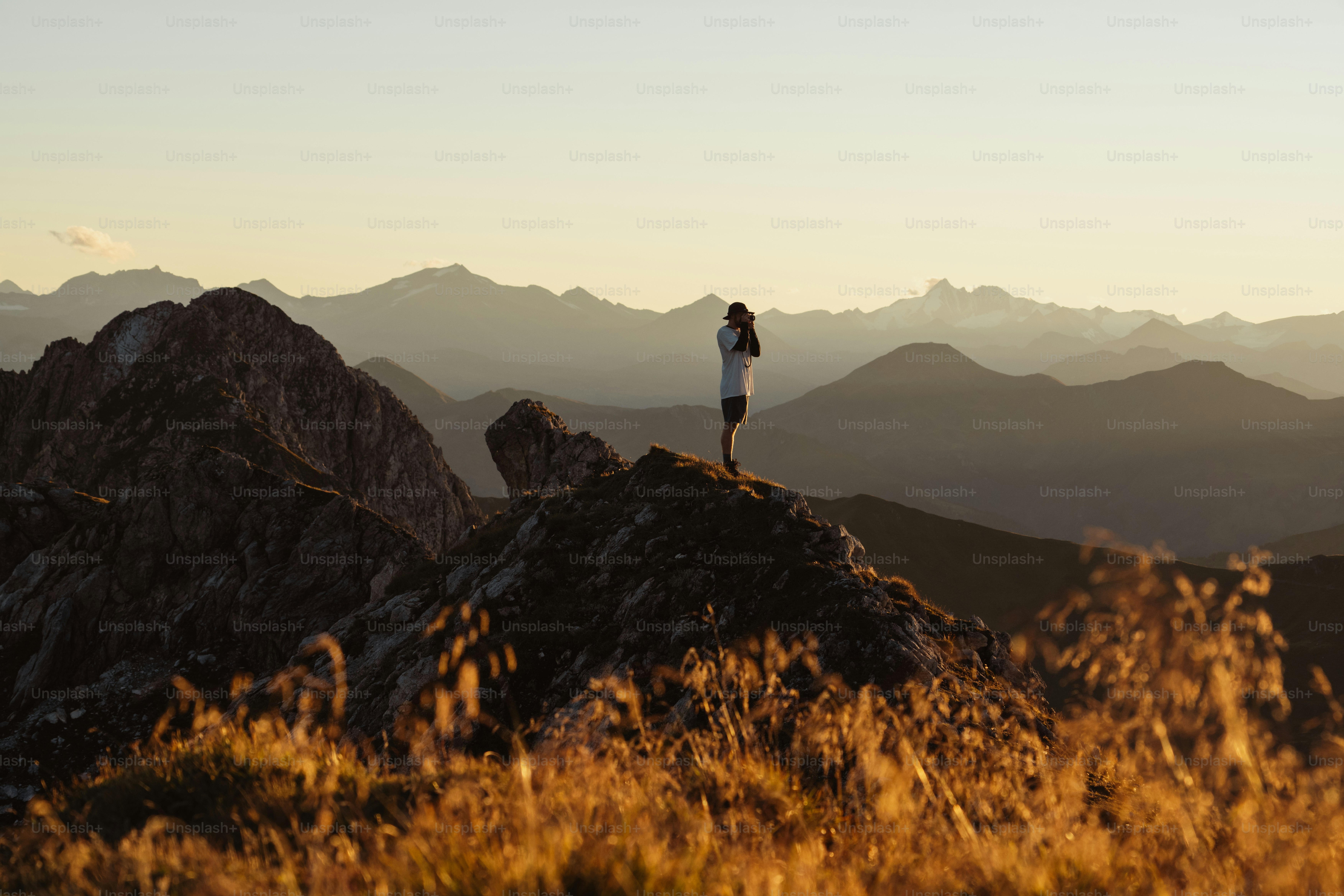A person stands on a rocky mountain peak at sunset.