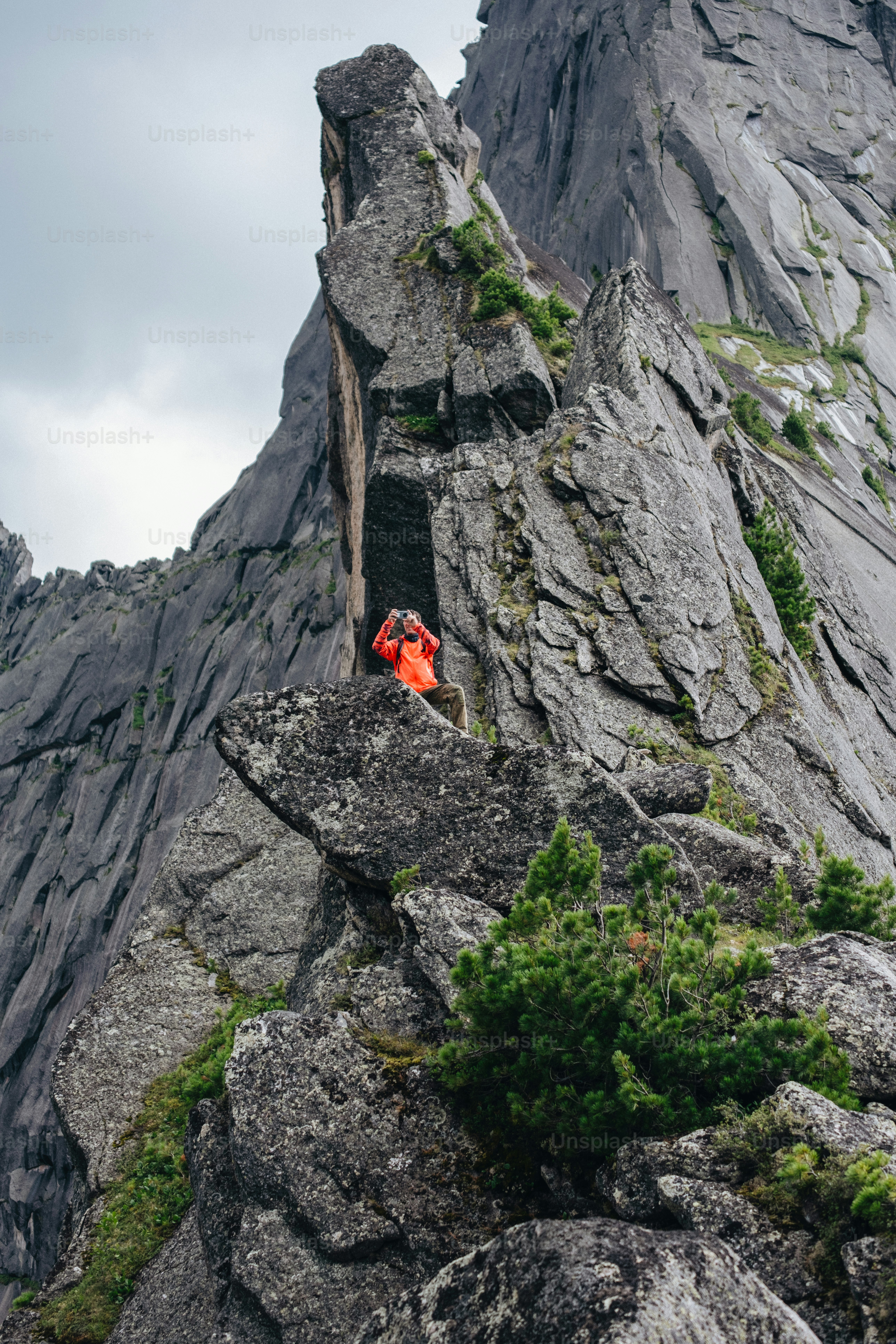 Hiker in orange jacket on a steep rocky mountain.