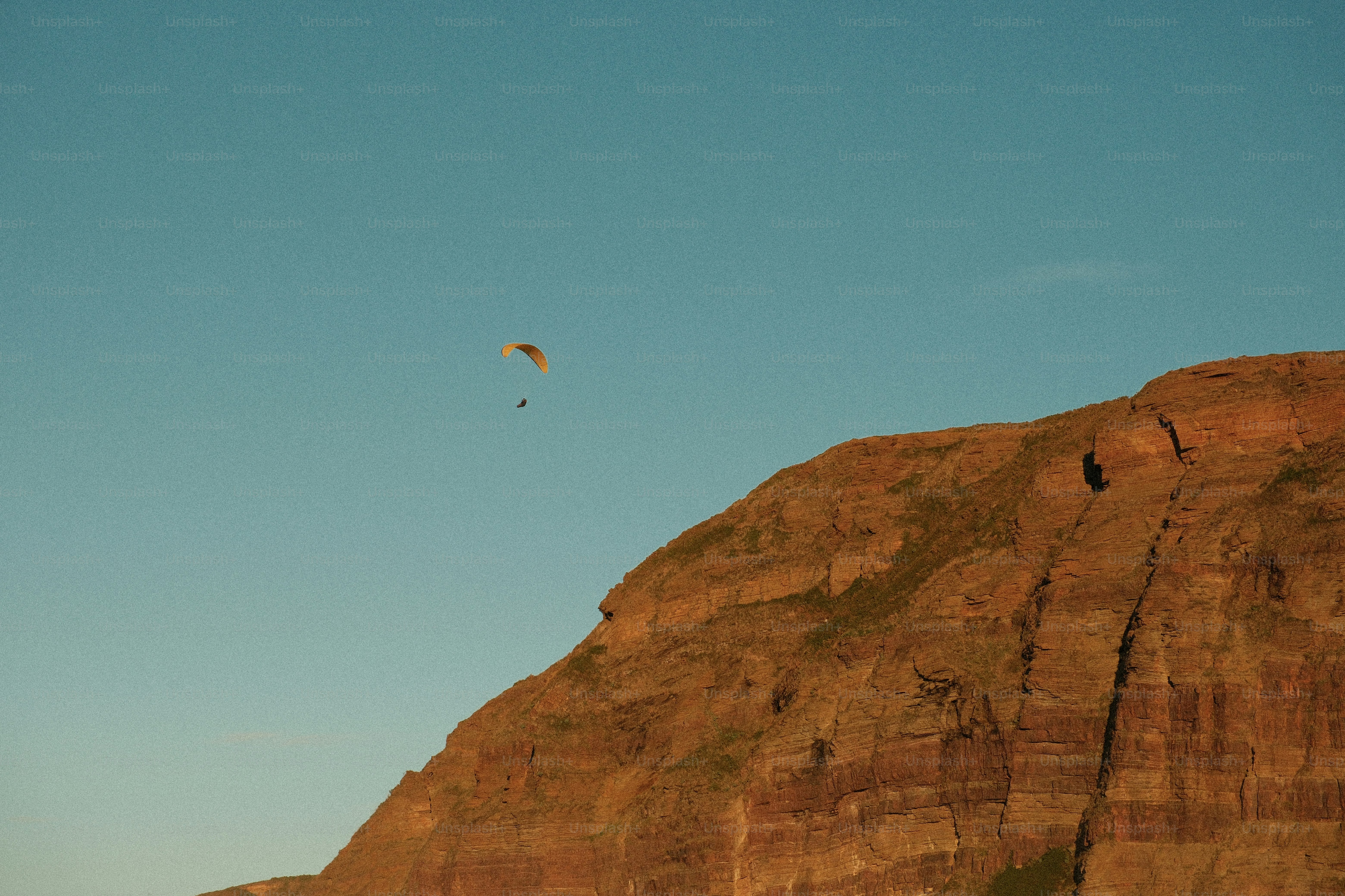 Paraglider flying near a rocky mountain cliffside mountain face