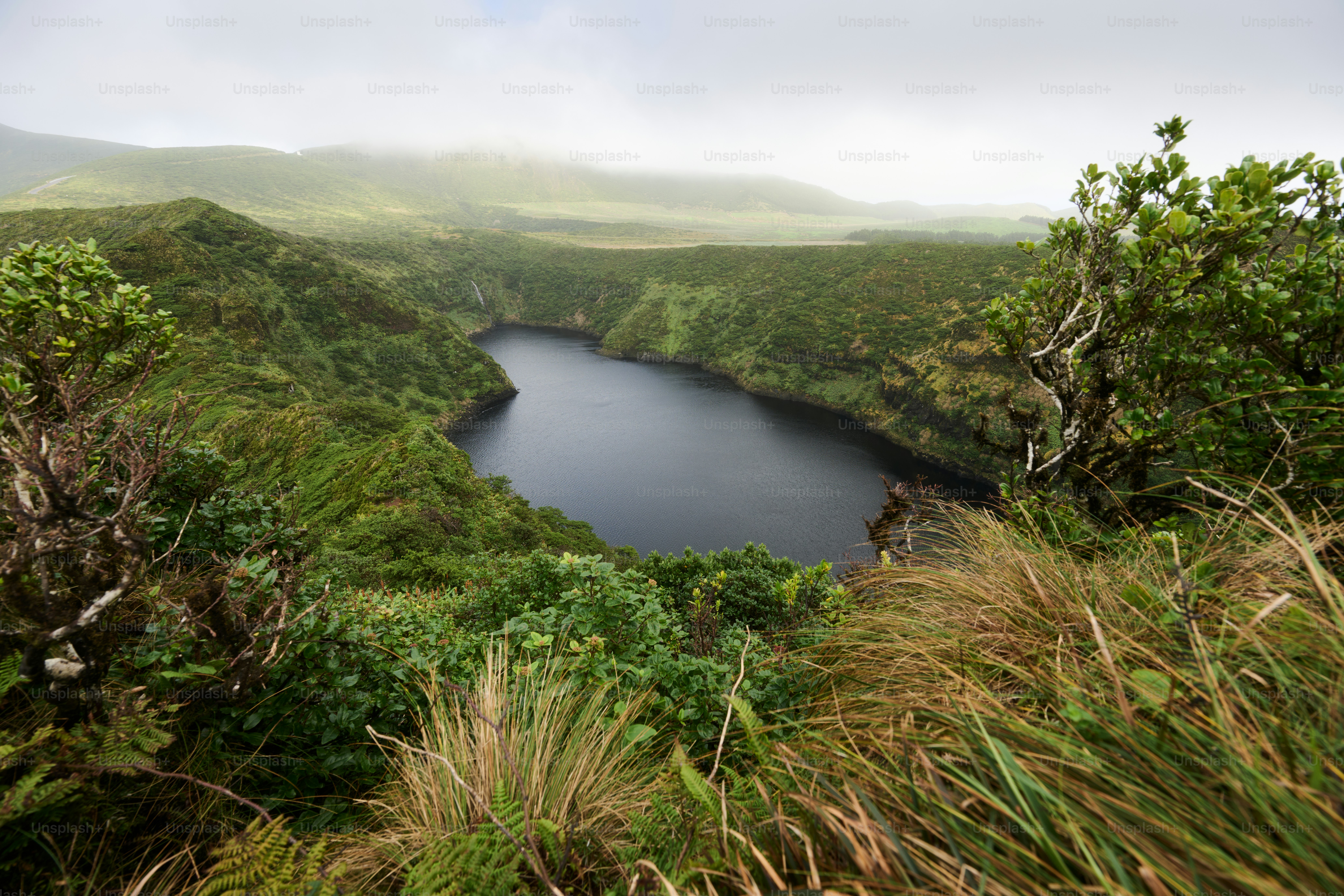 Lush green hills surround a dark, tranquil lake.