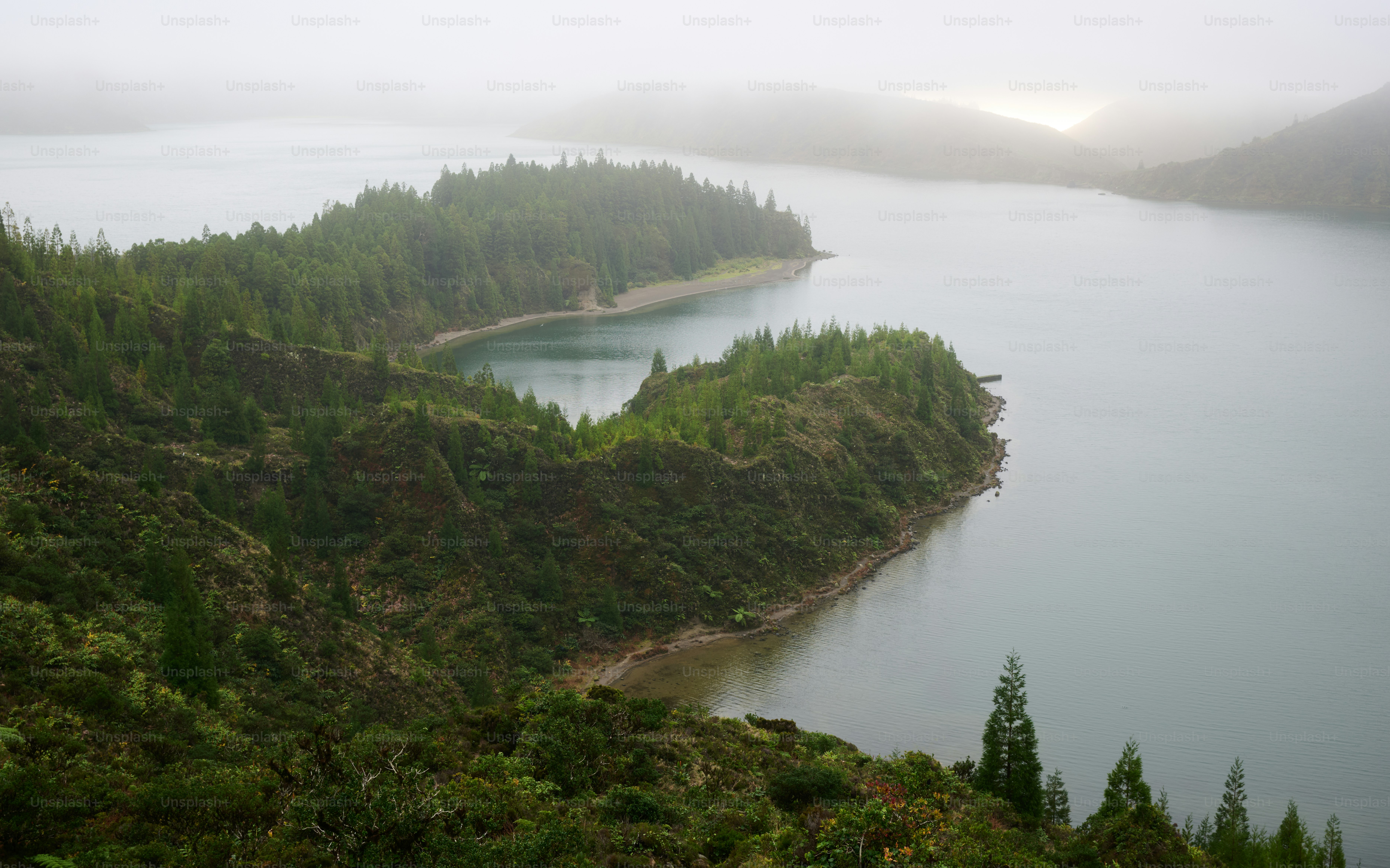 Misty lake surrounded by green, forested hillsides.