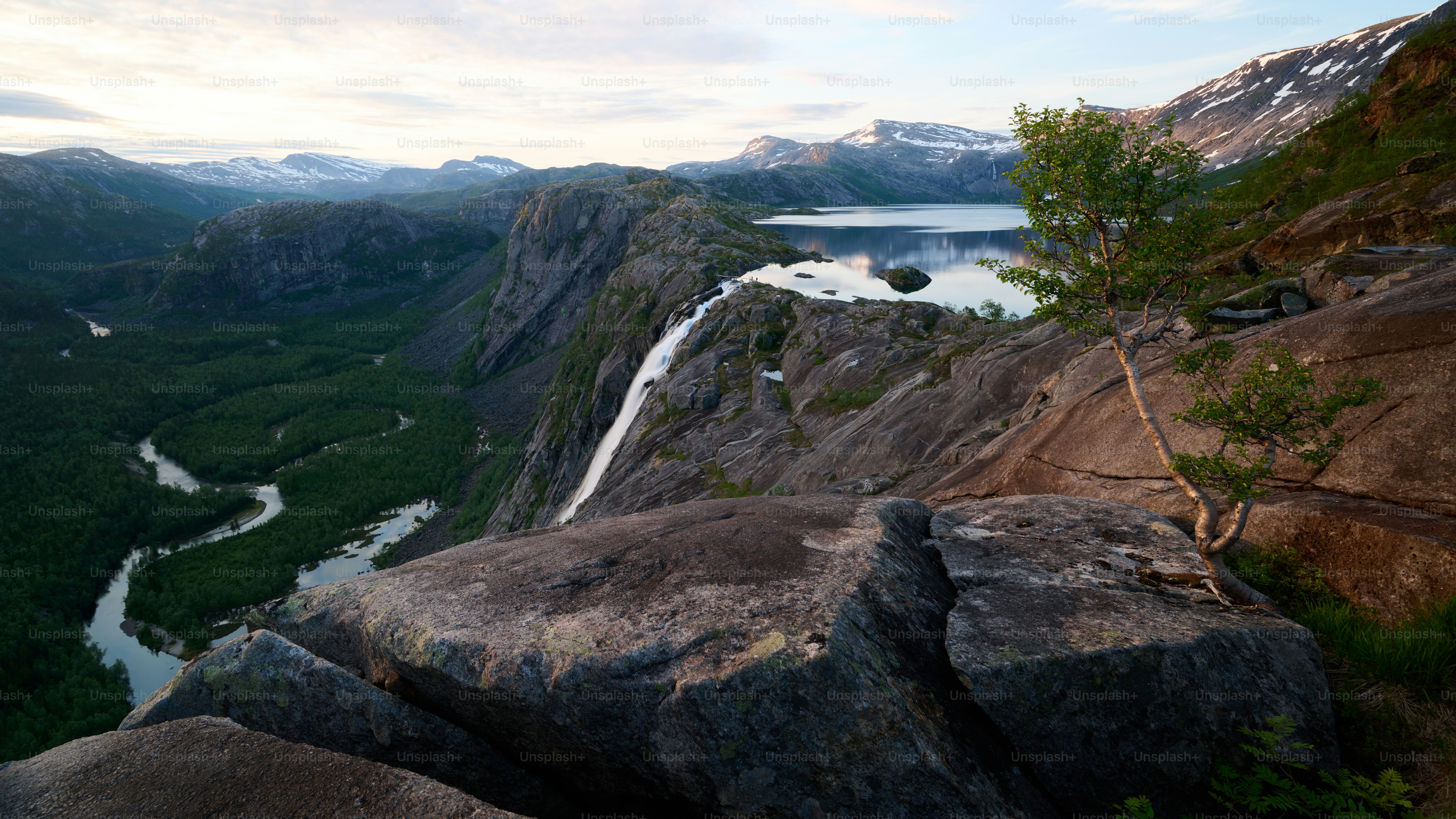 Felsige Klippe mit Blick auf ein üppig grünes Tal und einen See.