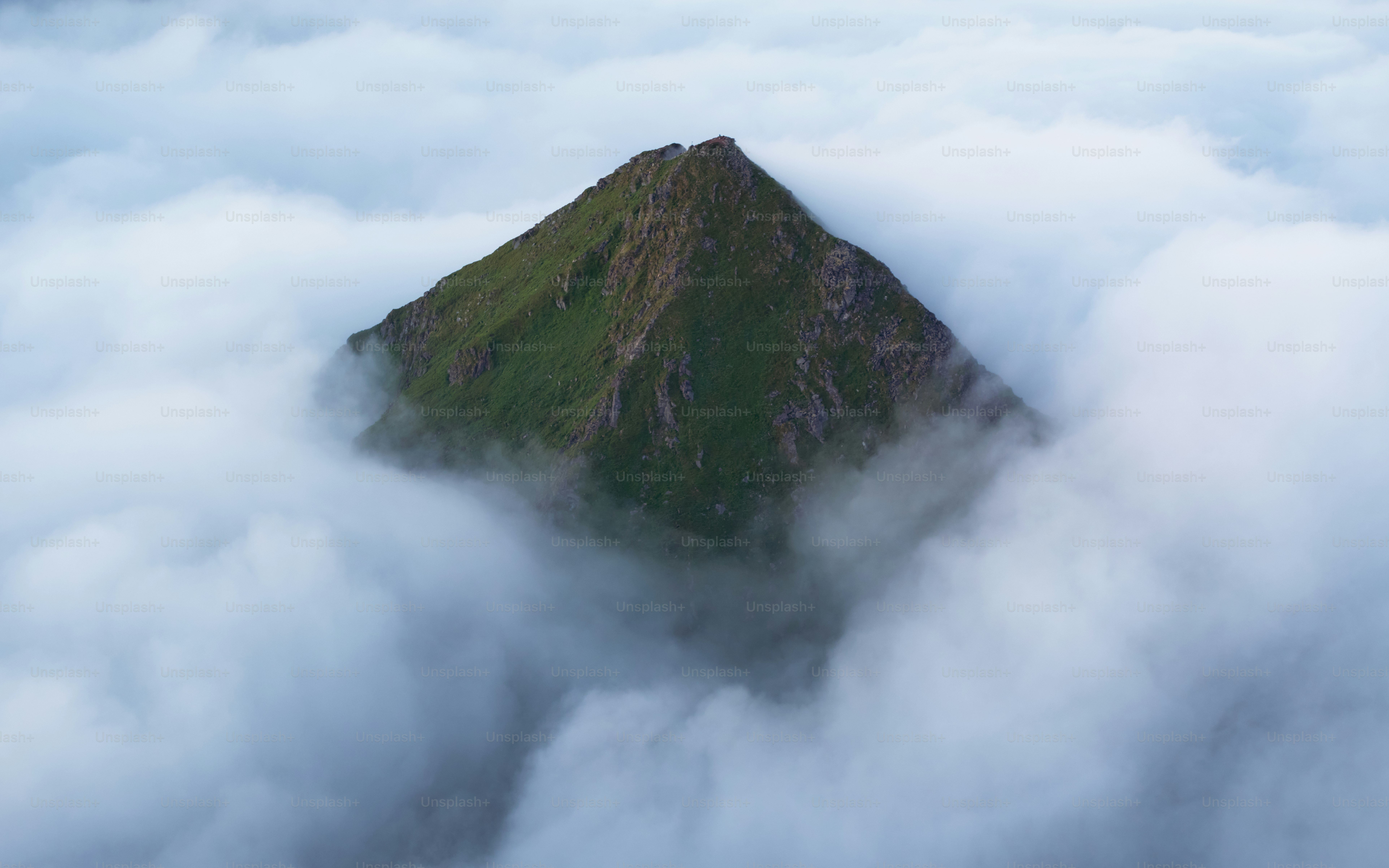 Ein einsamer Berggipfel erhebt sich aus weichen Wolken.
