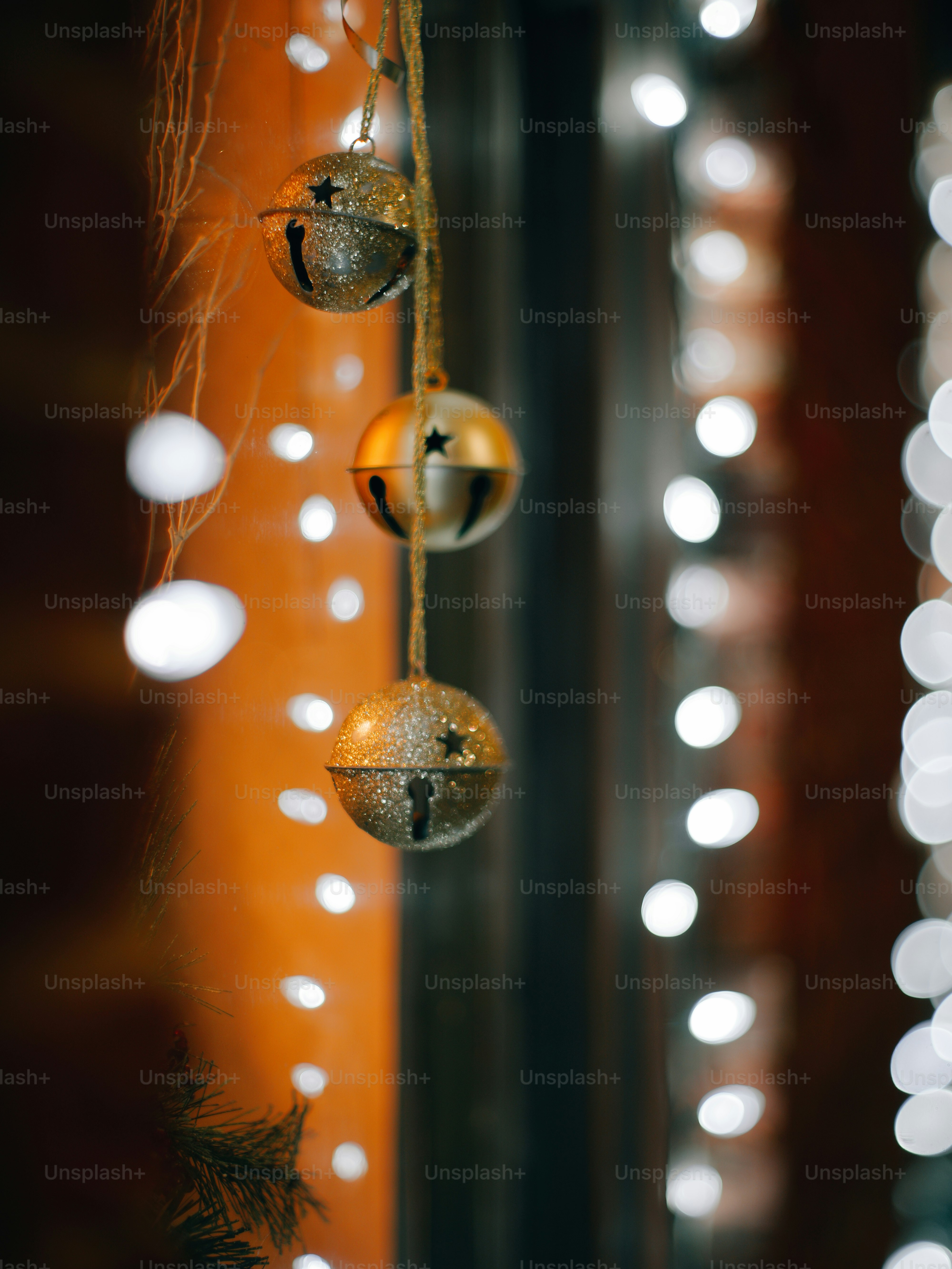 Three golden bells hang with blurred lights behind.
