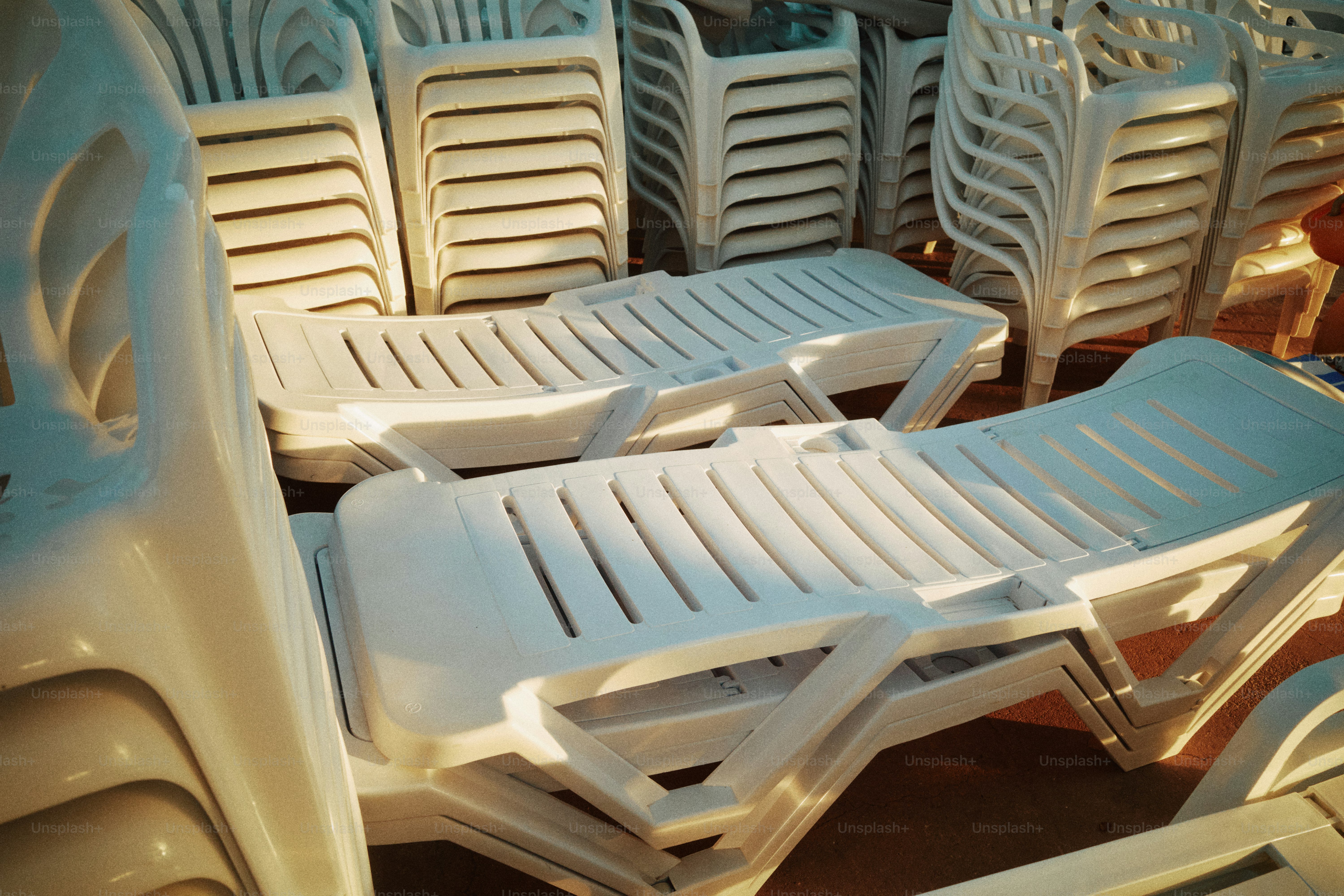 Stacked white plastic lounge chairs on a sunny day