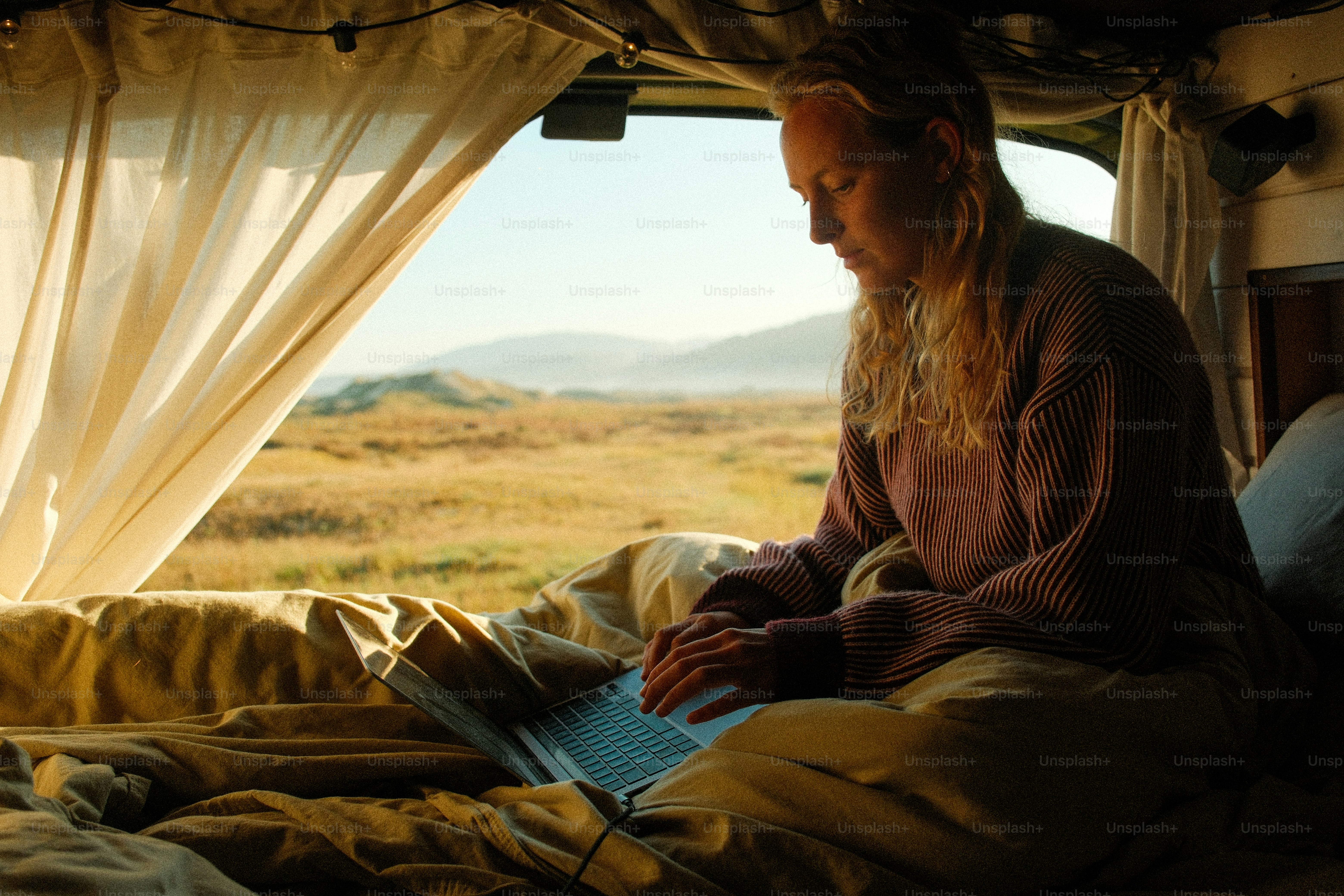 Woman working on laptop inside camper van with scenic view.