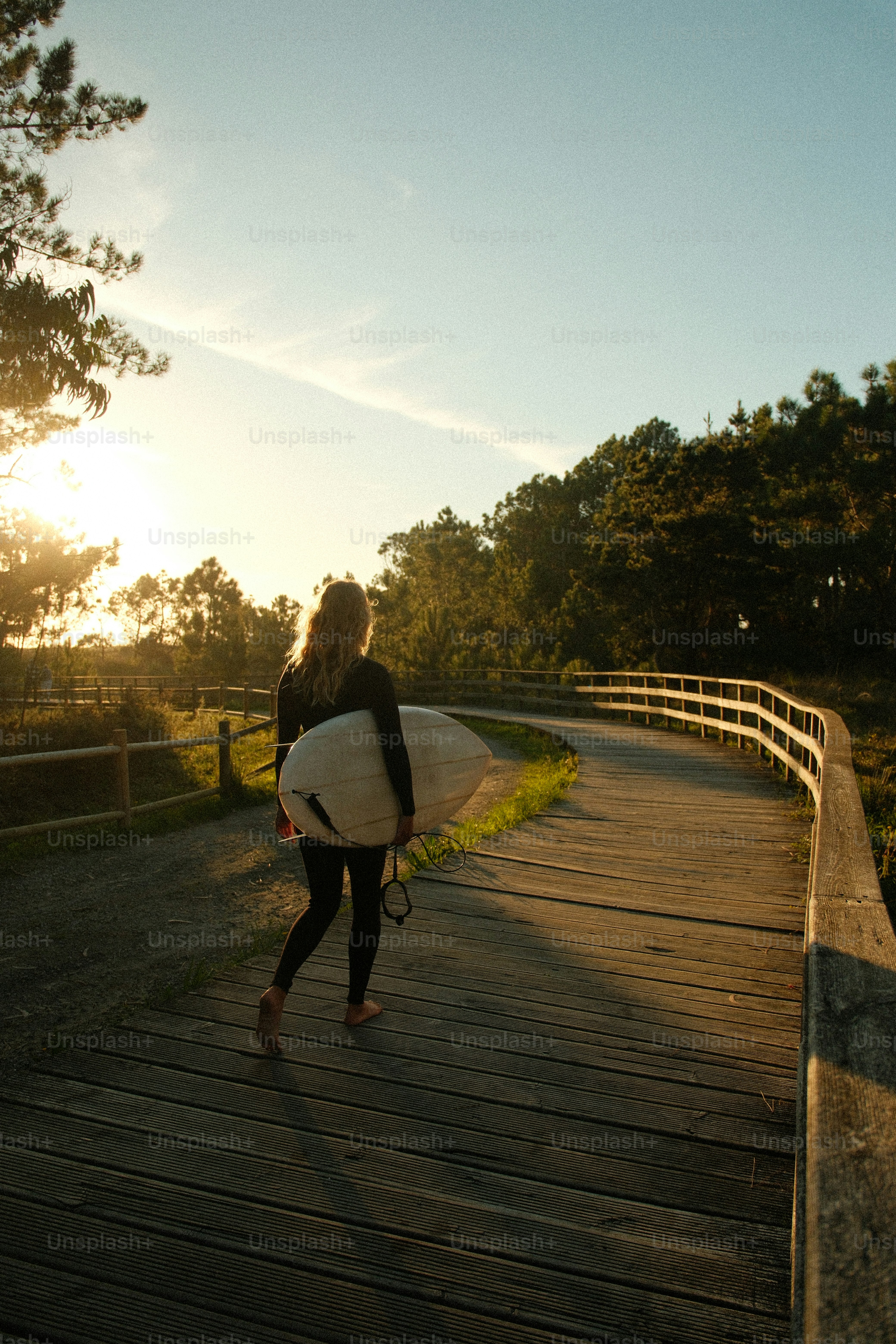 Woman in wetsuit carrying surfboard on wooden path