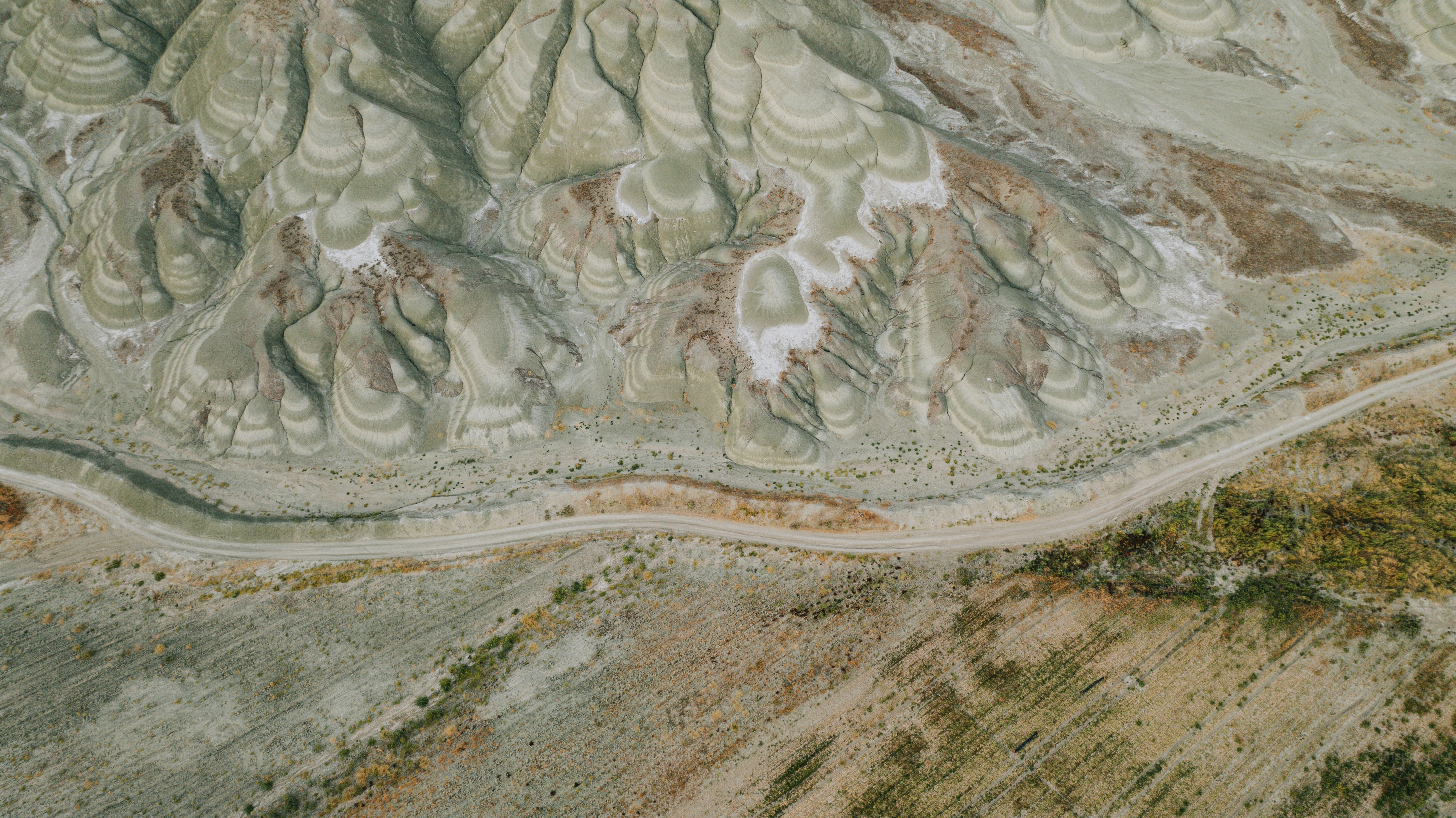 Aerial view of colorful desert badlands with a dirt road.