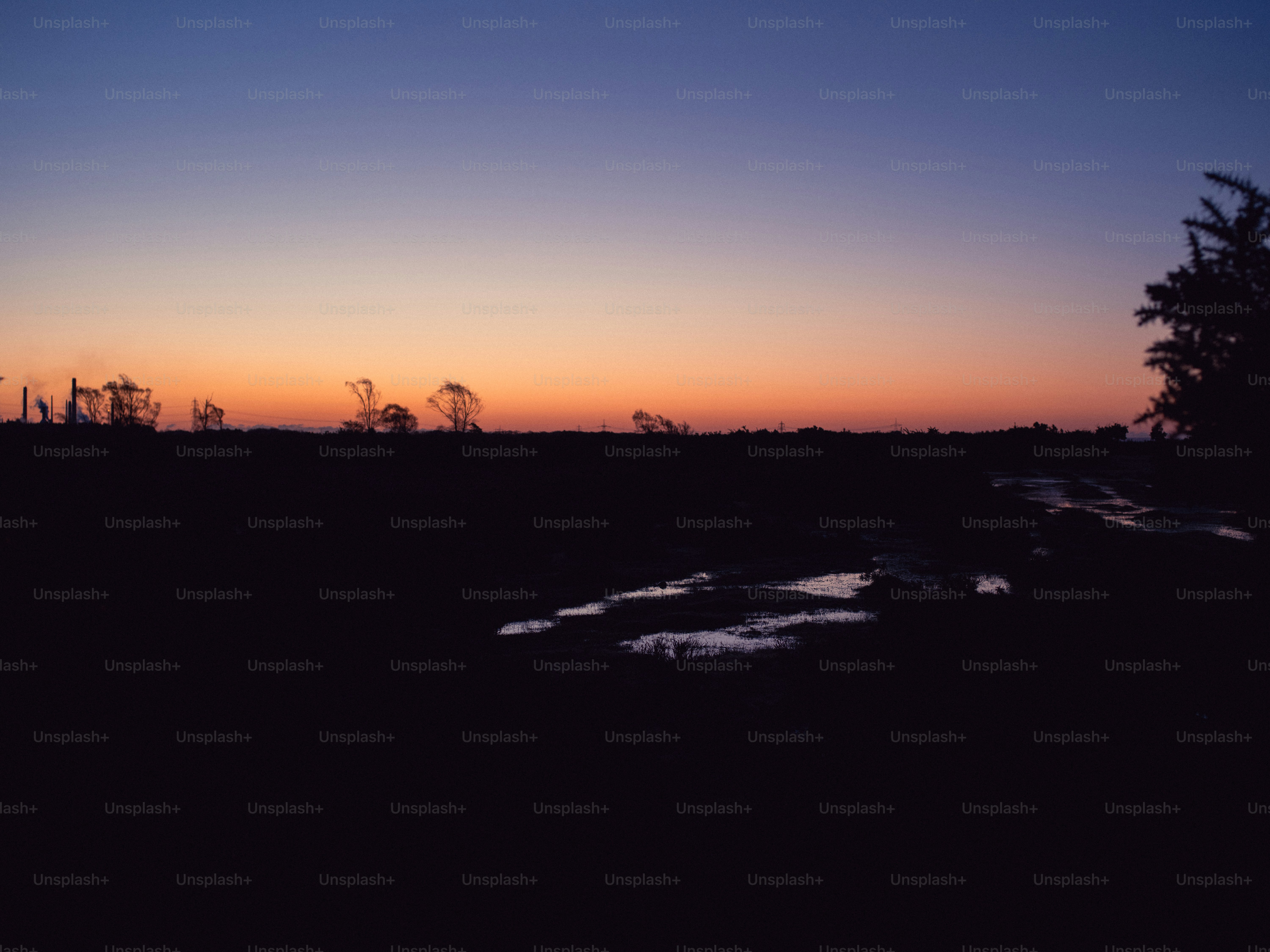 Sunset over a dark, flat landscape with puddles.