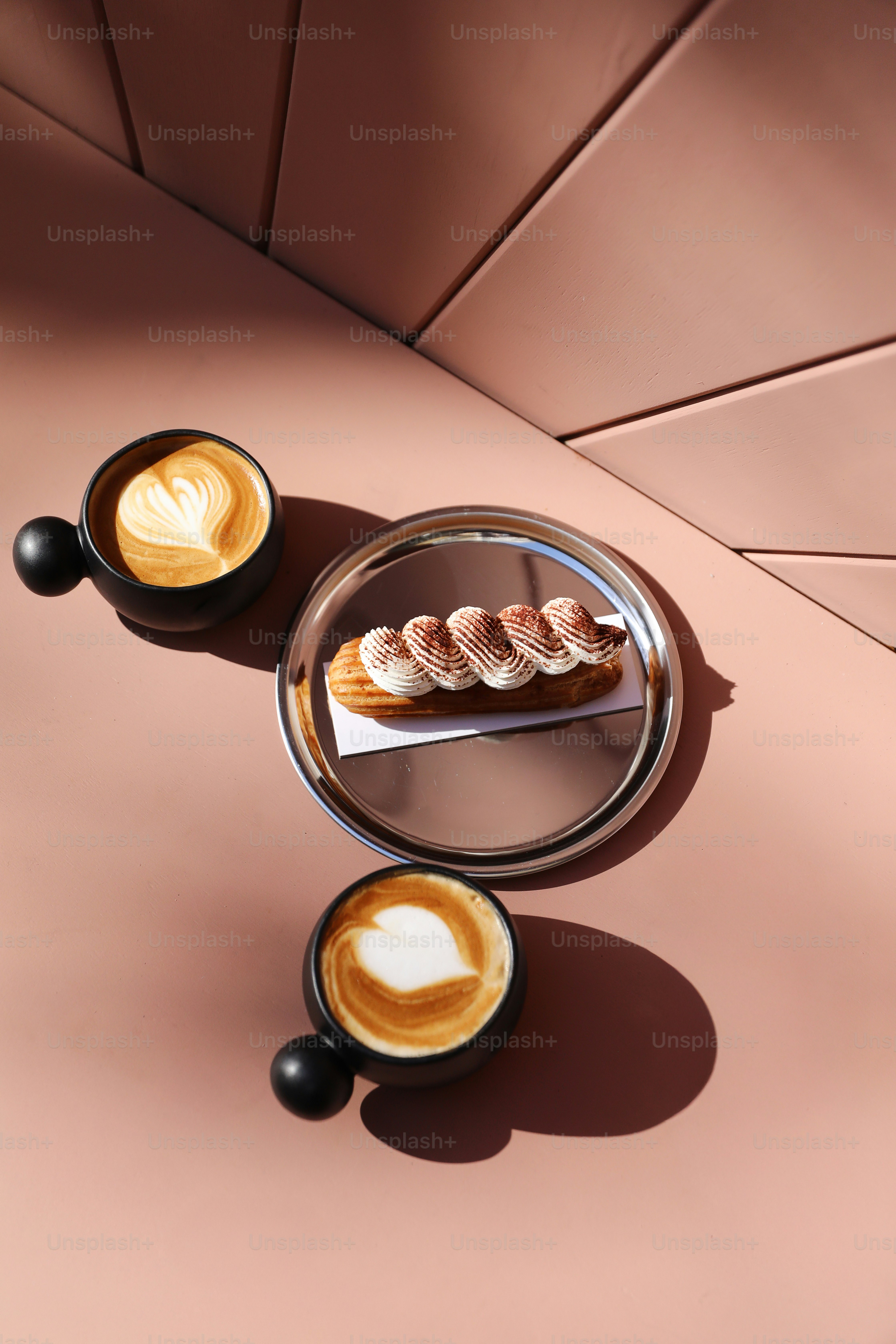 Deux cafés et un éclair sur une surface rose.