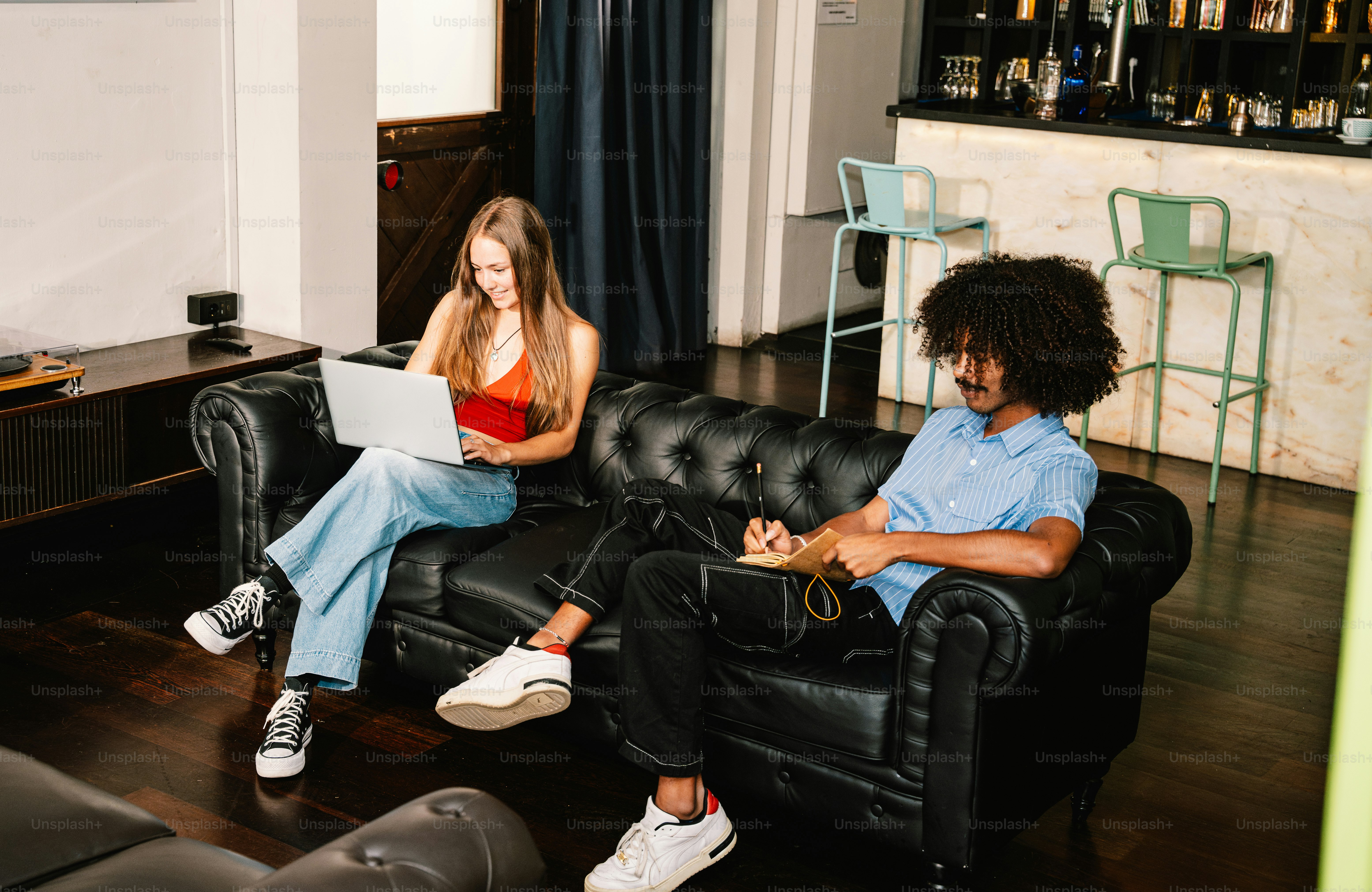 Zwei Personen sitzen auf einem Ledersofa und benutzen Laptops.
