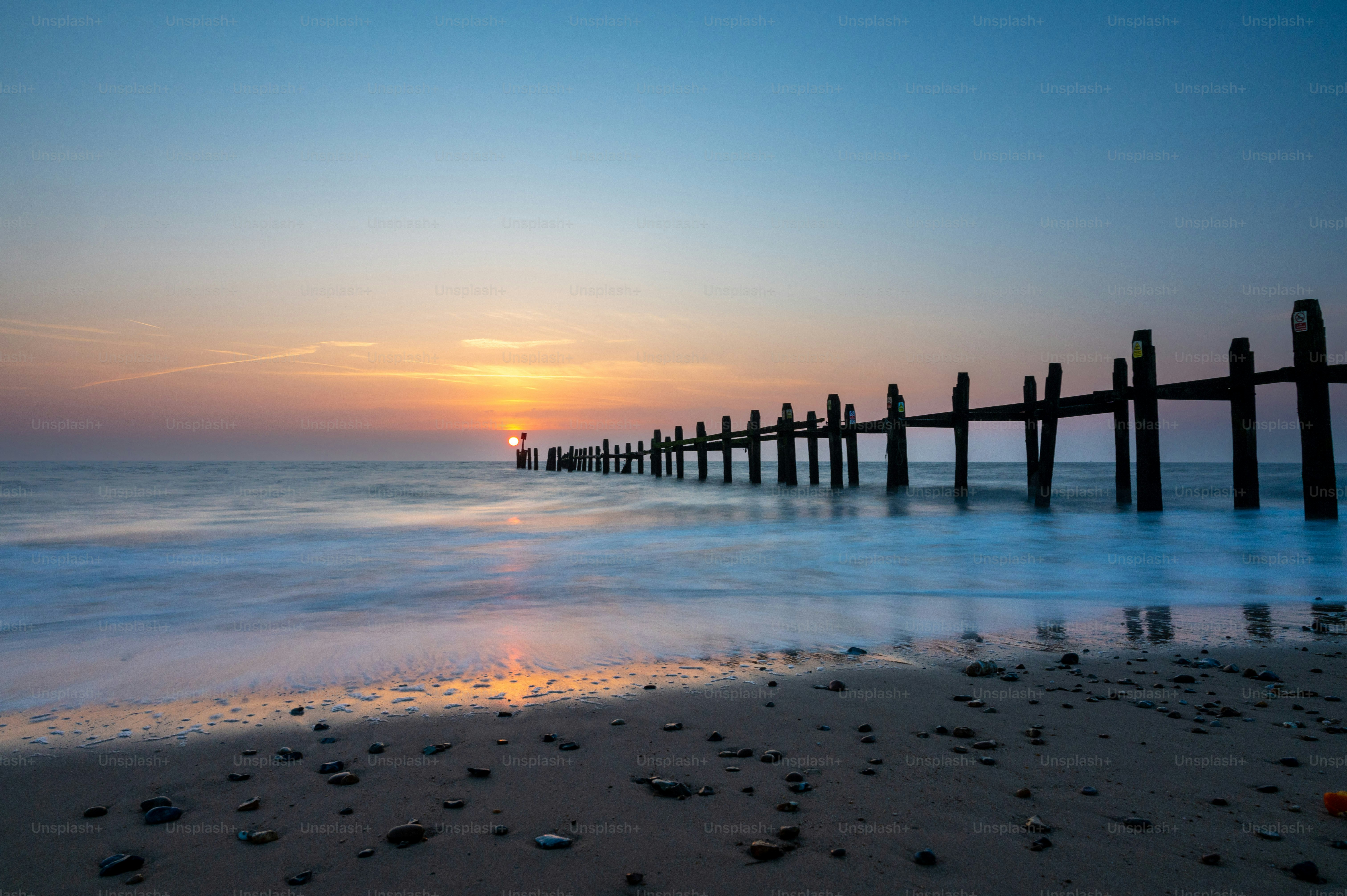 Sunset over the ocean with a weathered pier.