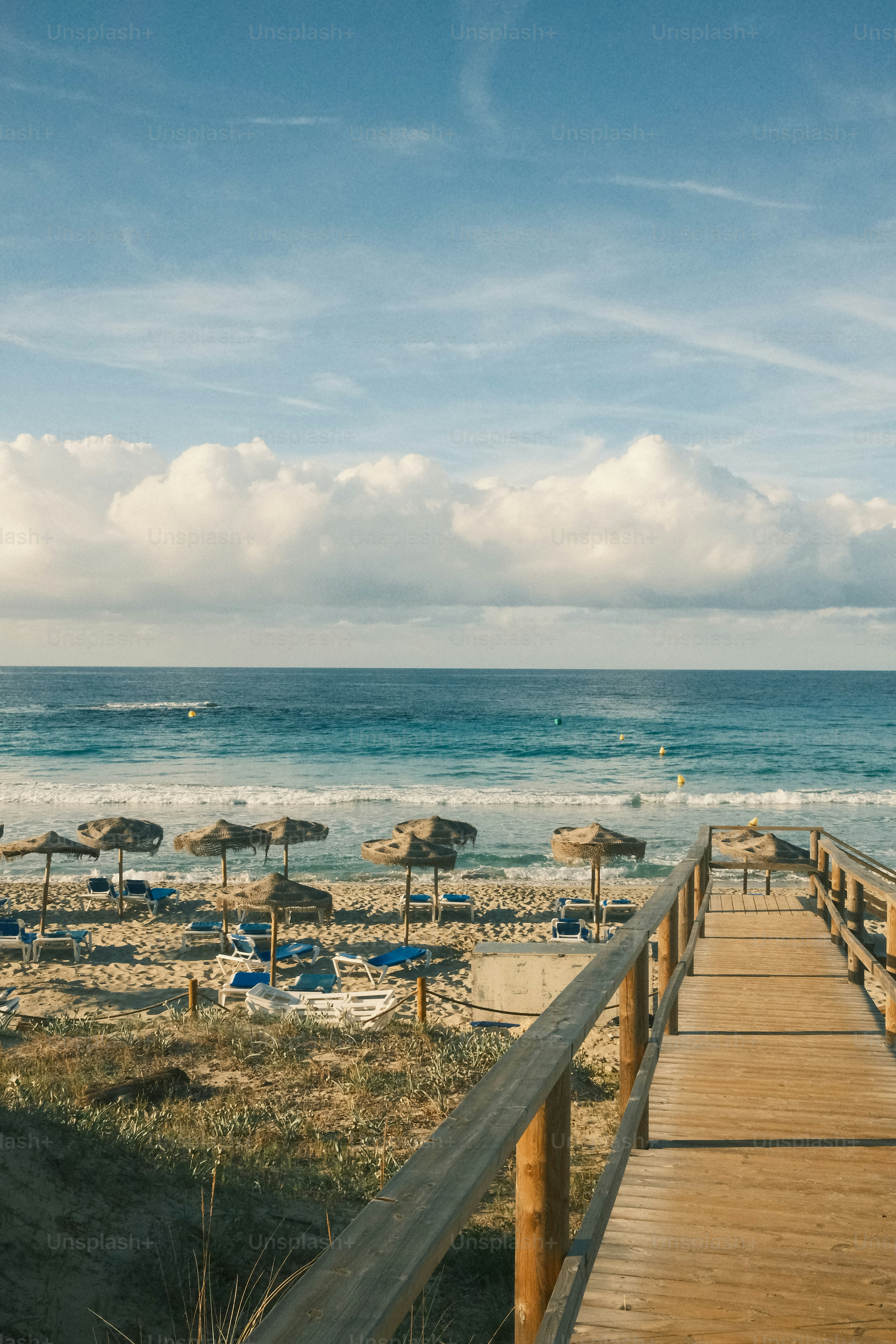Wooden walkway leading to a beach with umbrellas and ocean.