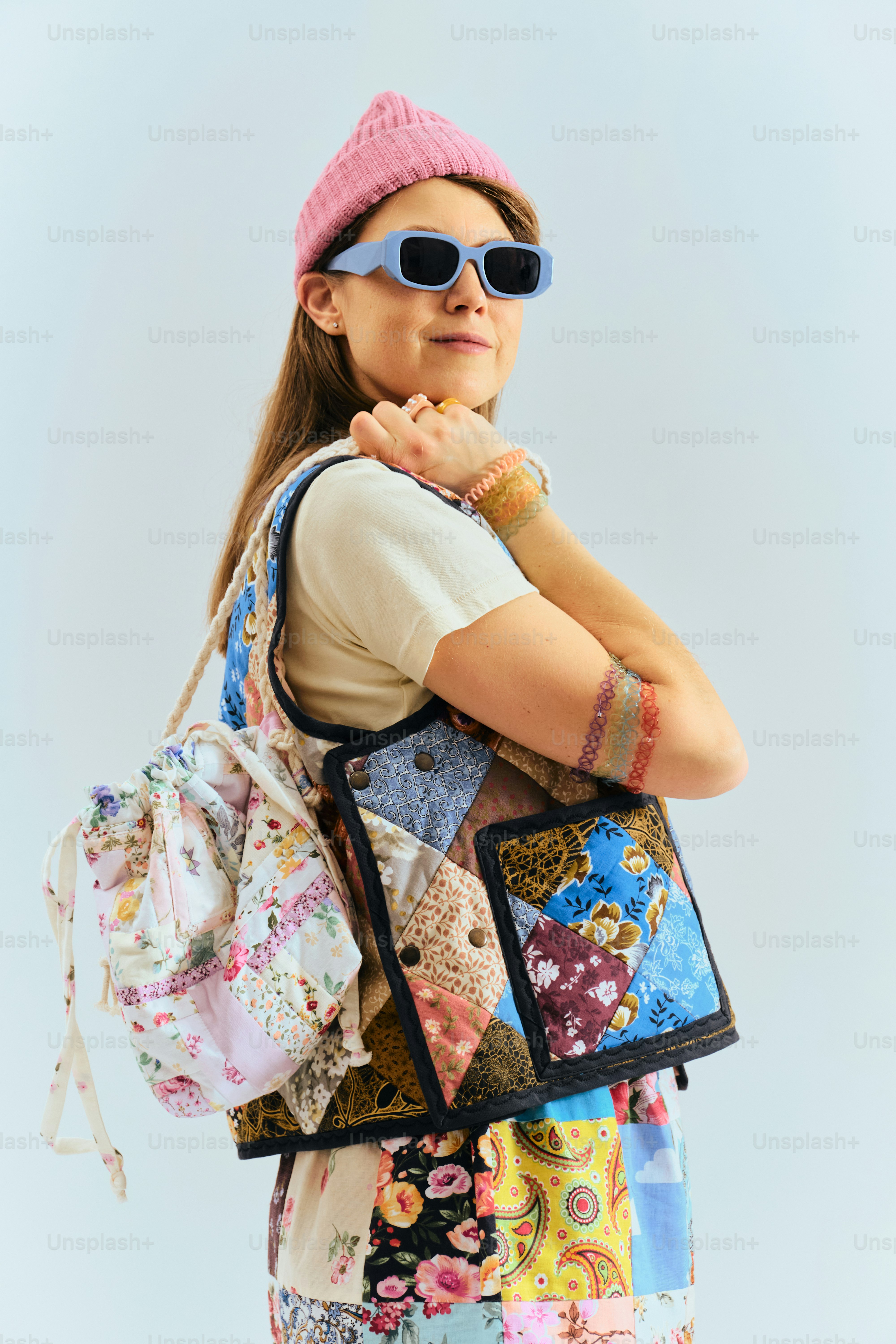 Woman wearing a pink beanie, sunglasses, and patchwork vest