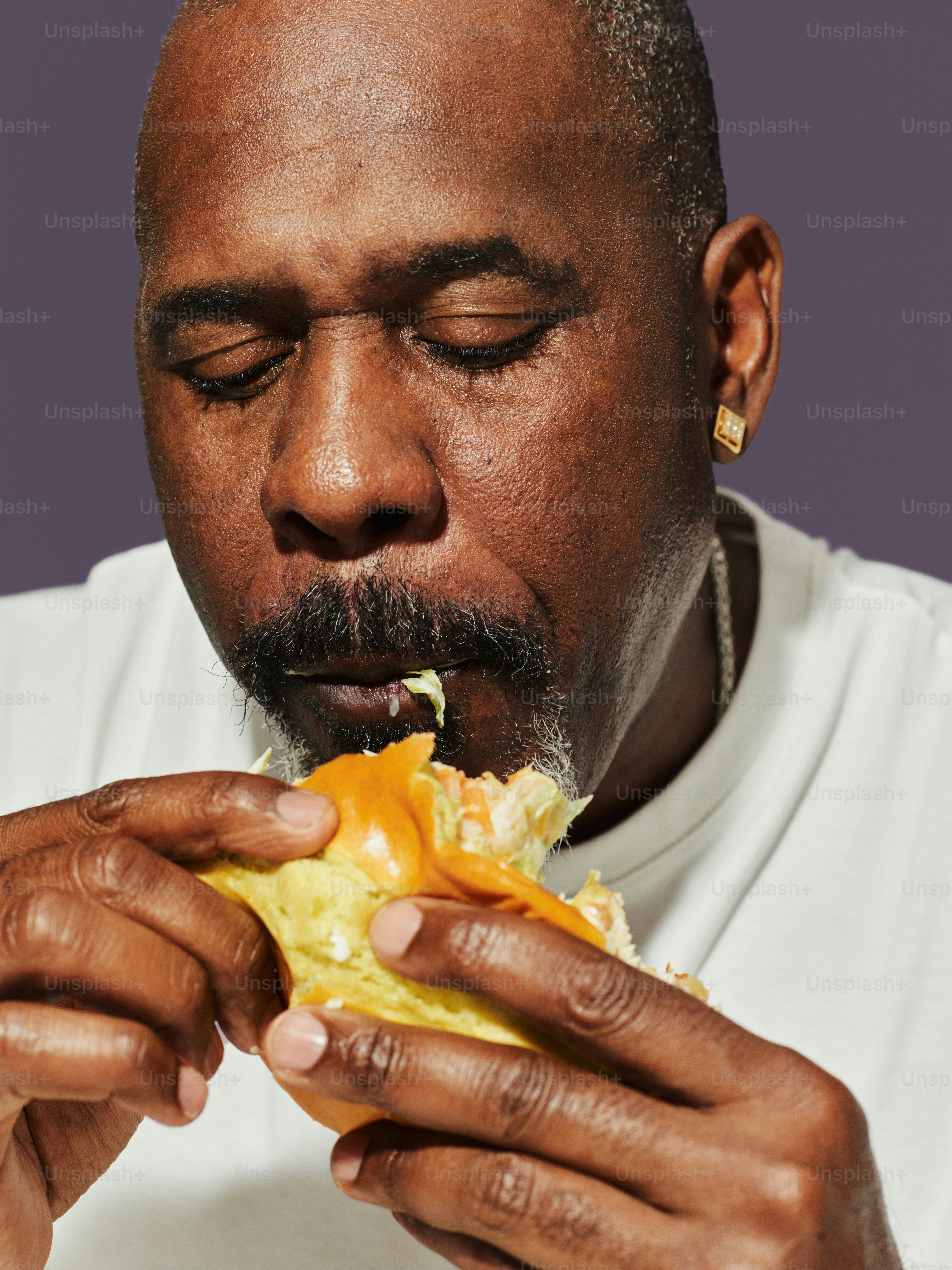 Man with eyes closed eating a sandwich