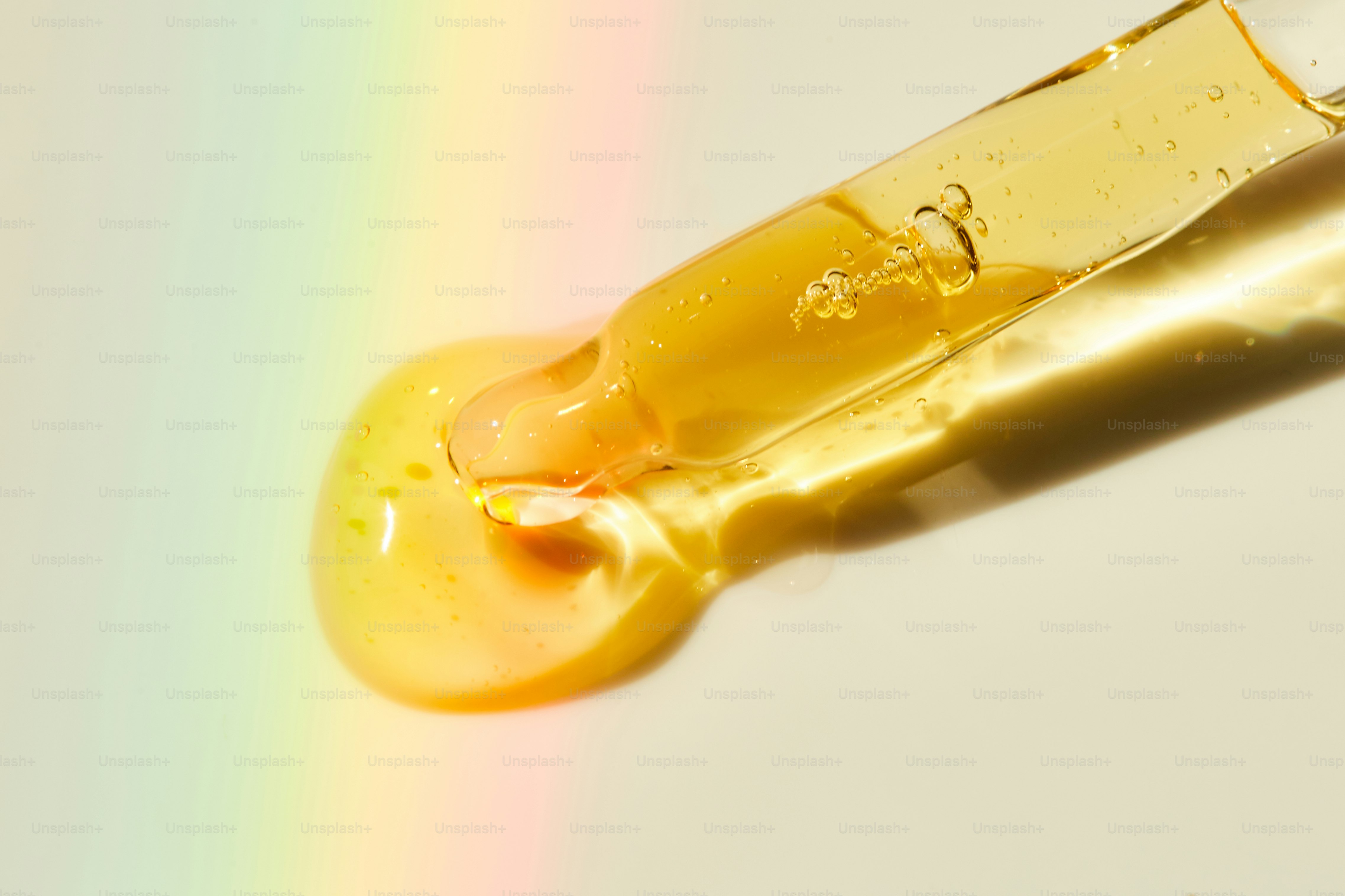 Un cuentagotas que libera un líquido amarillo con reflejos arcoíris.