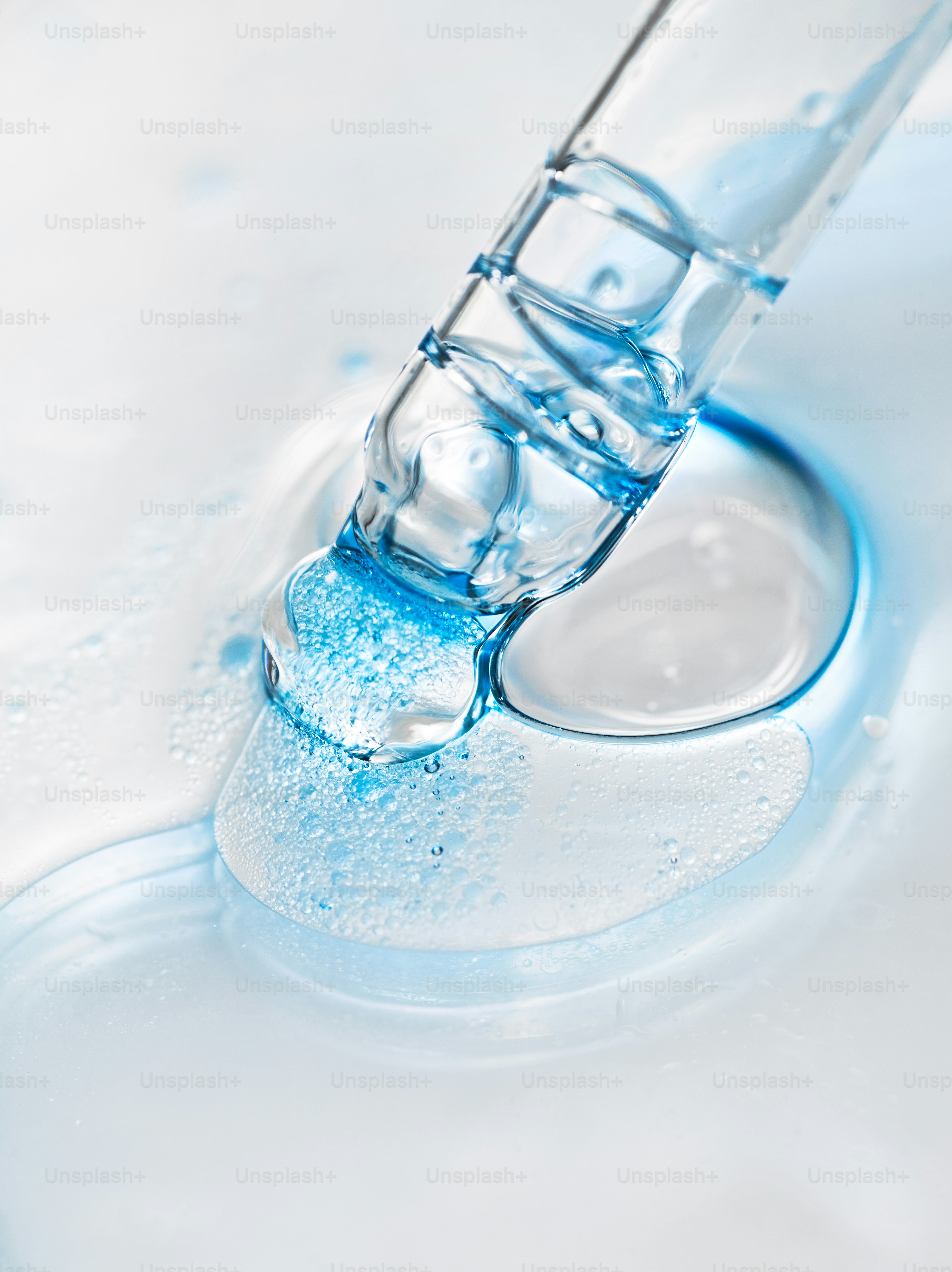 A dropper releasing blue liquid onto a white surface.
