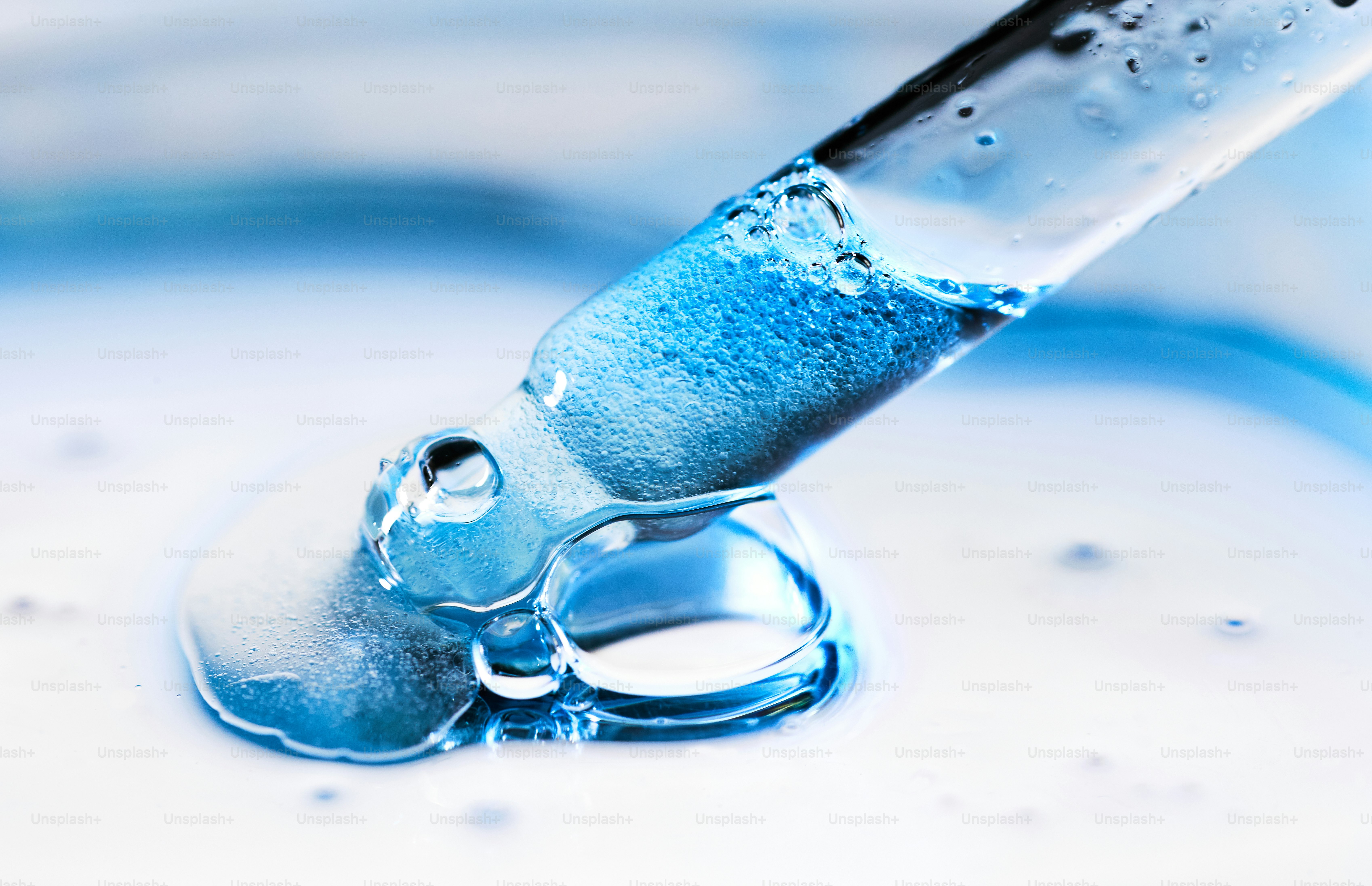 Blue liquid dripping from a glass pipette.