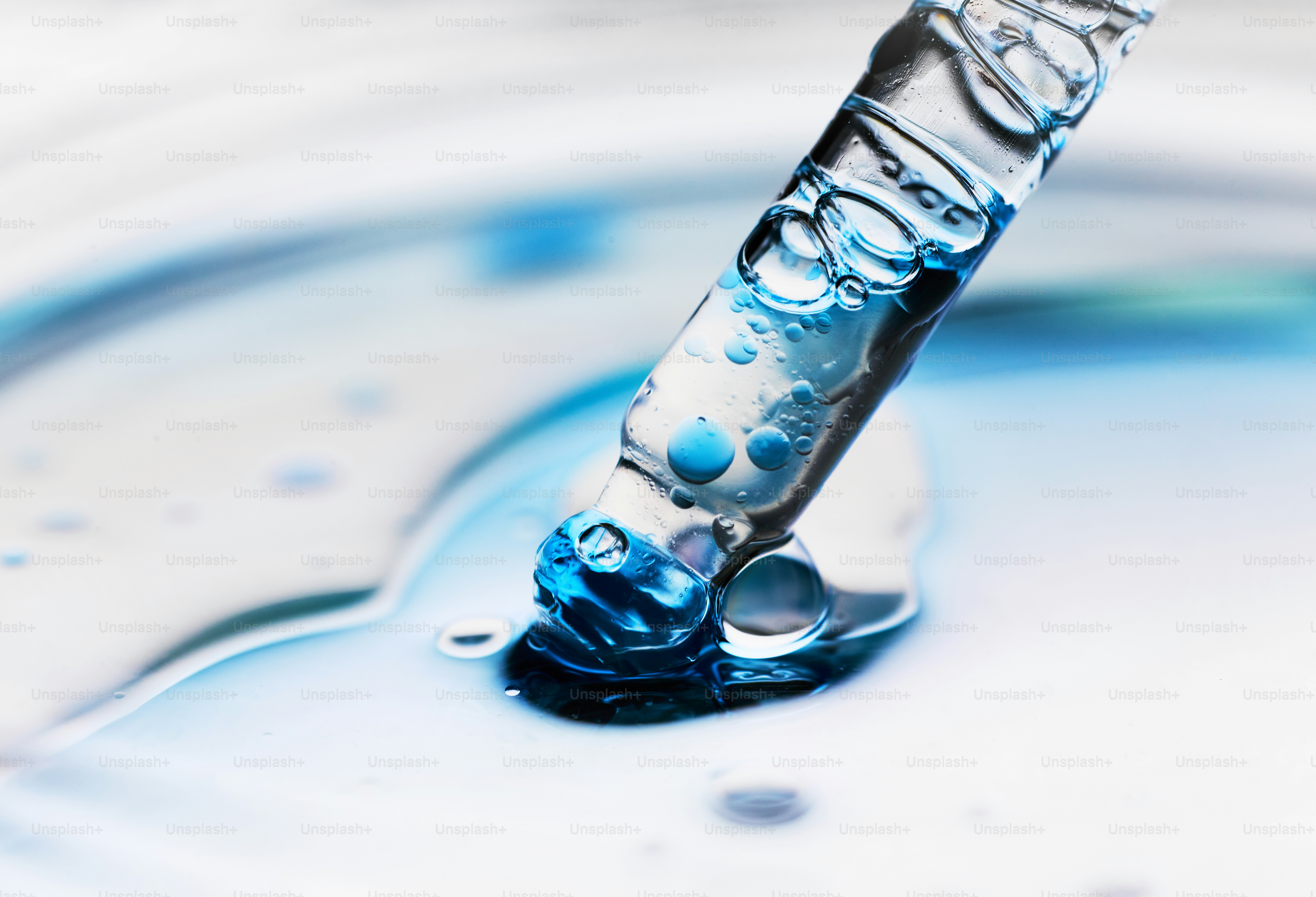 A close-up of a pipette dripping blue liquid into water.
