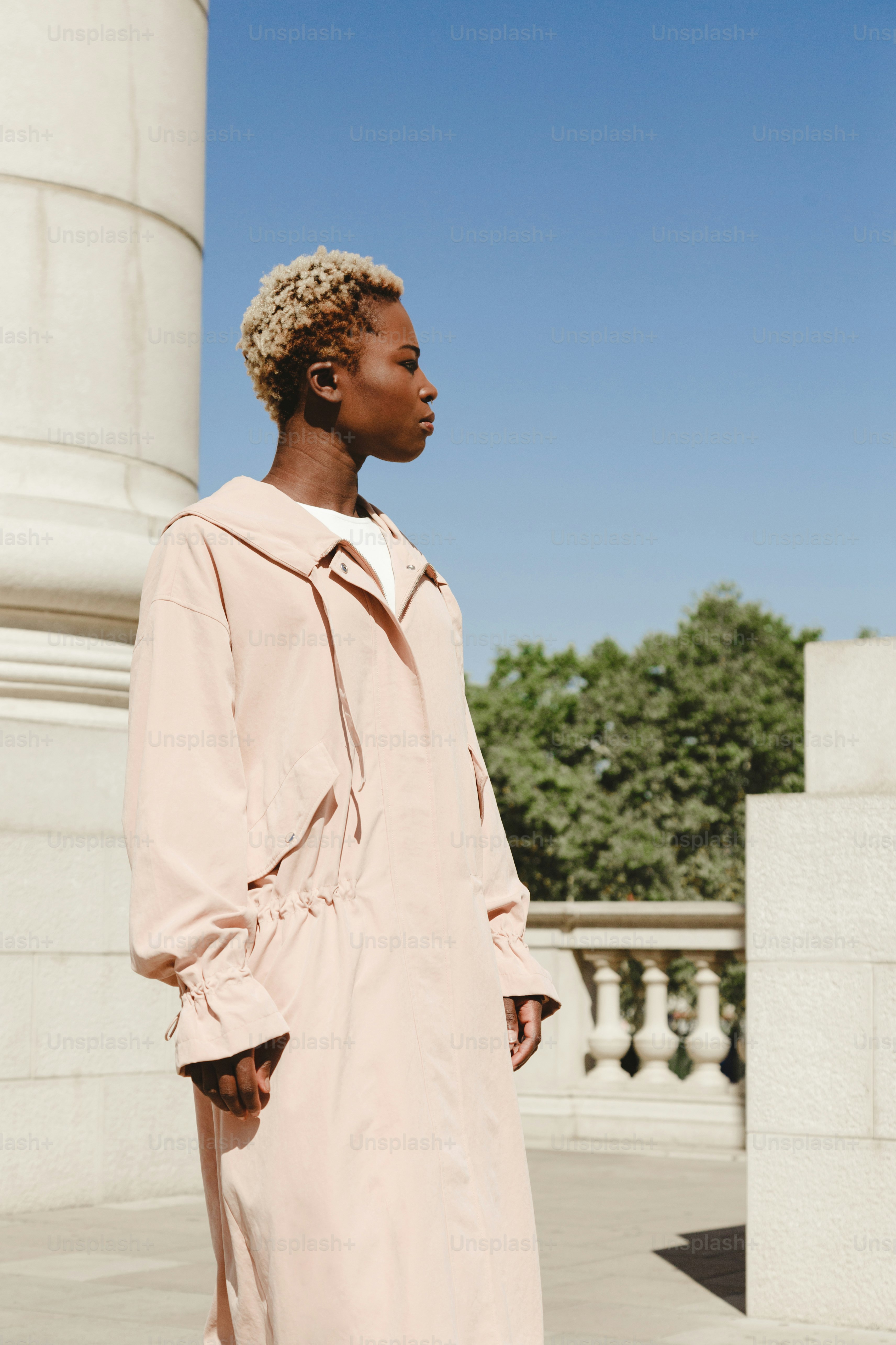 Woman in a light pink coat stands outdoors.