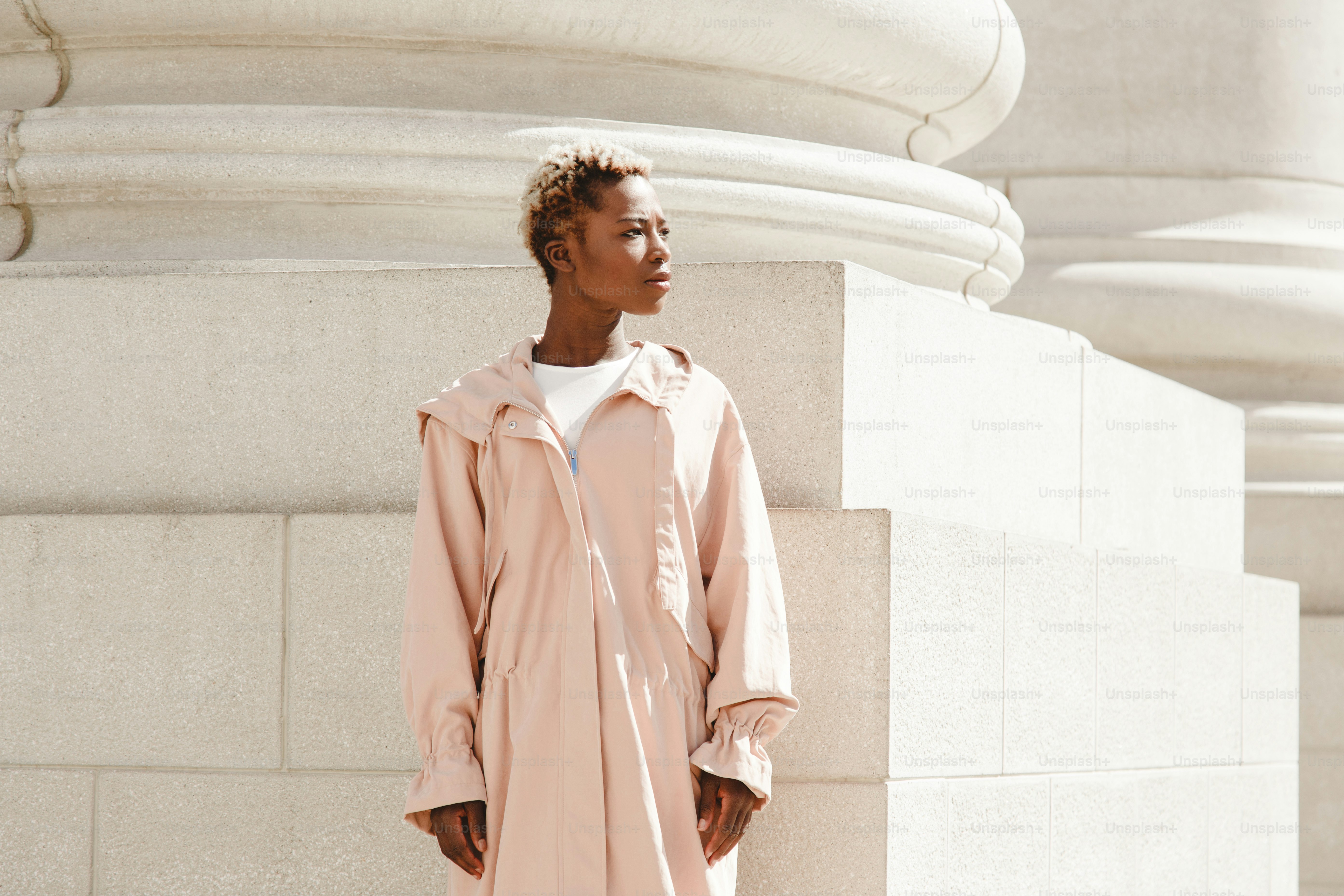 Woman in pink coat stands by classical architecture.