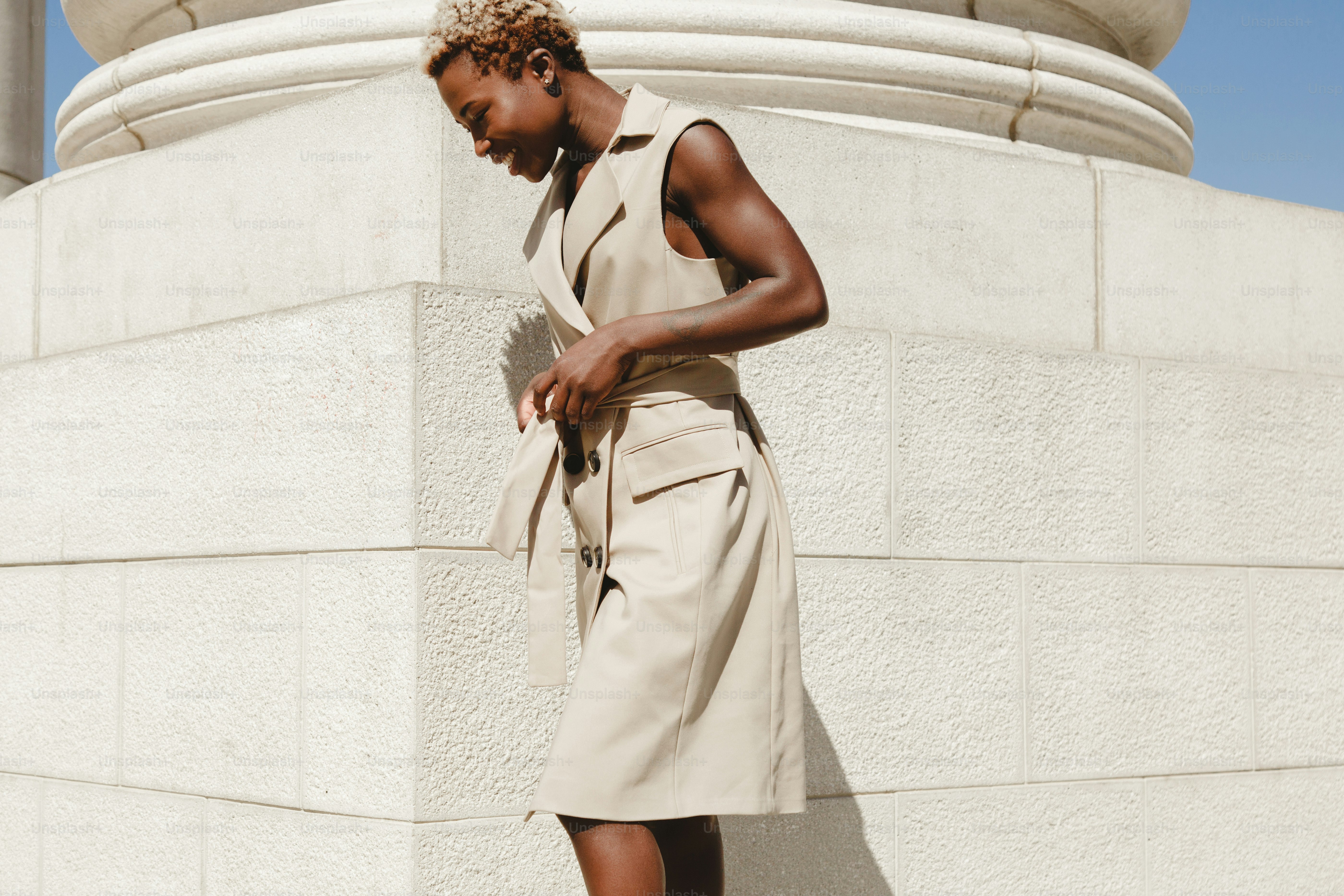 Woman in tan sleeveless dress by stone column