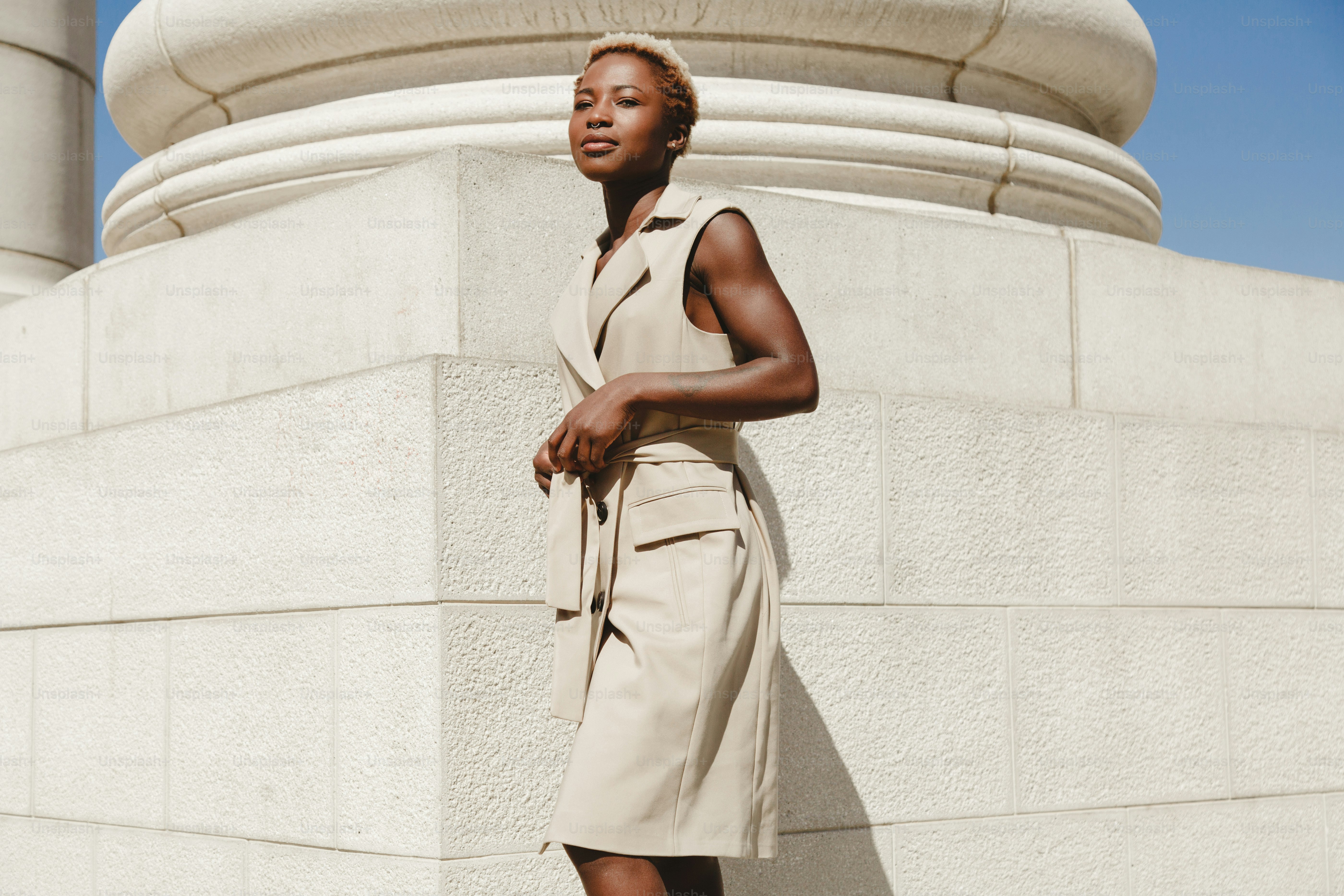 A woman in a tan dress stands by a column.