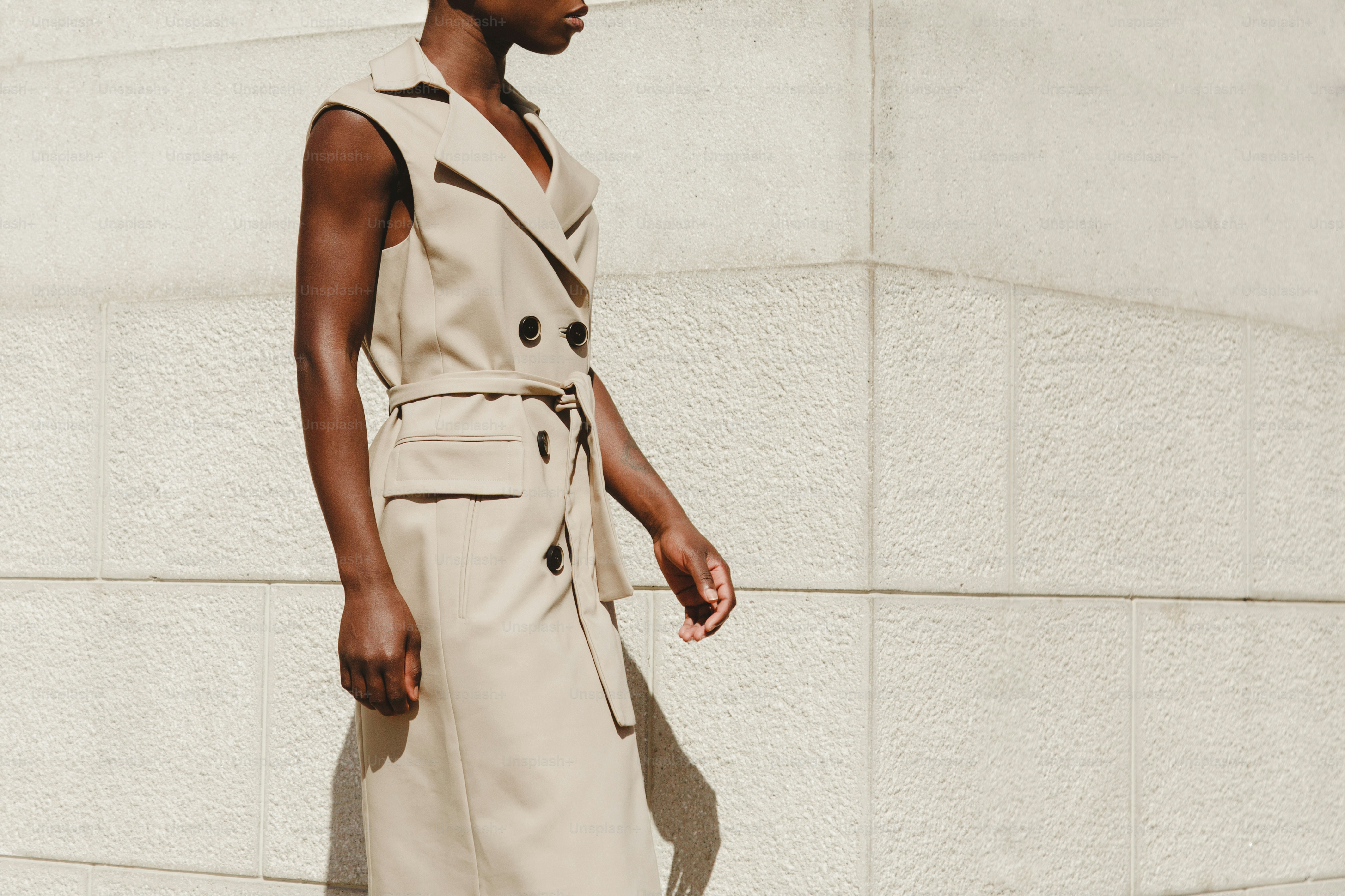 Woman in a beige trench coat walks by a wall.