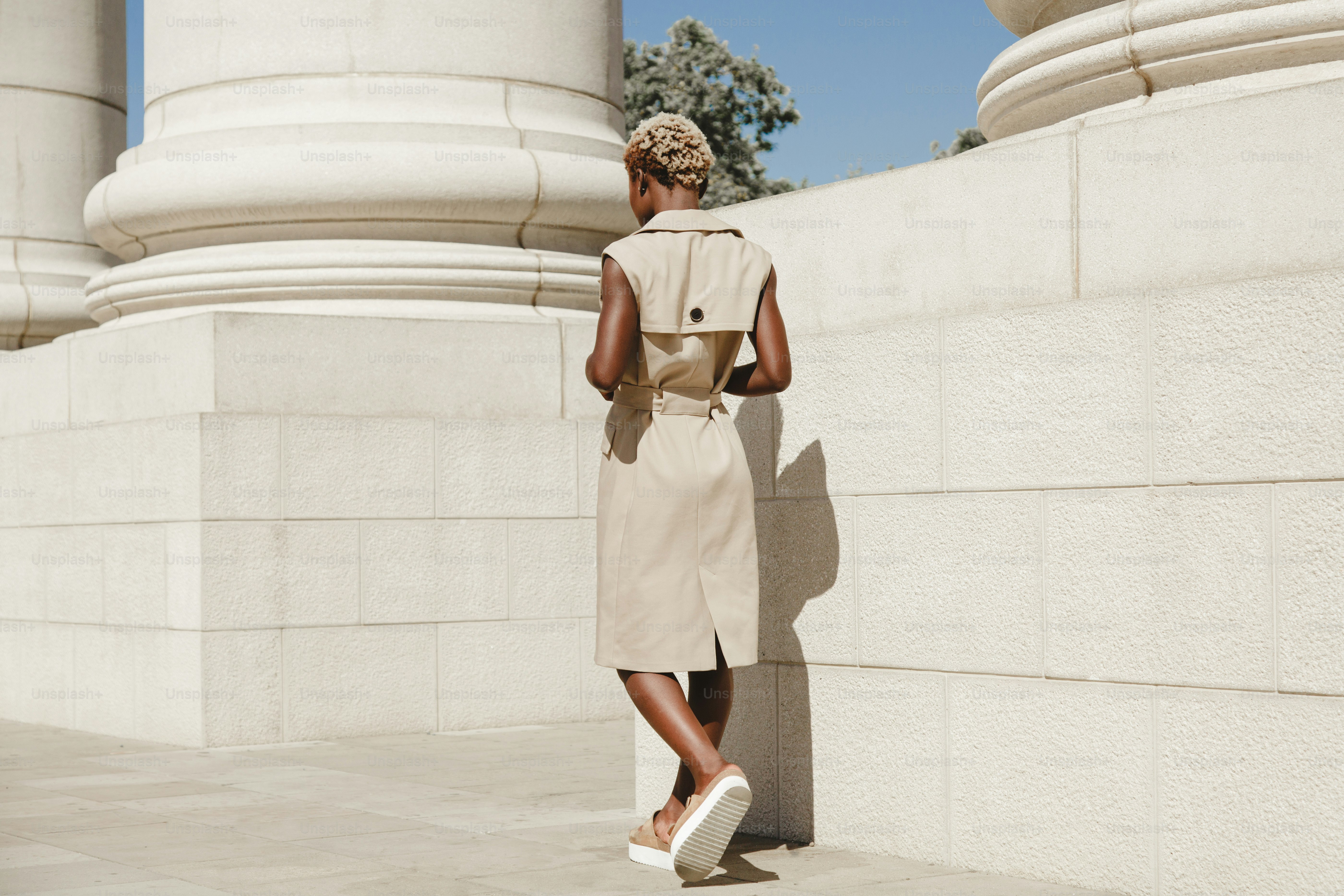 Woman in a beige dress stands near columns
