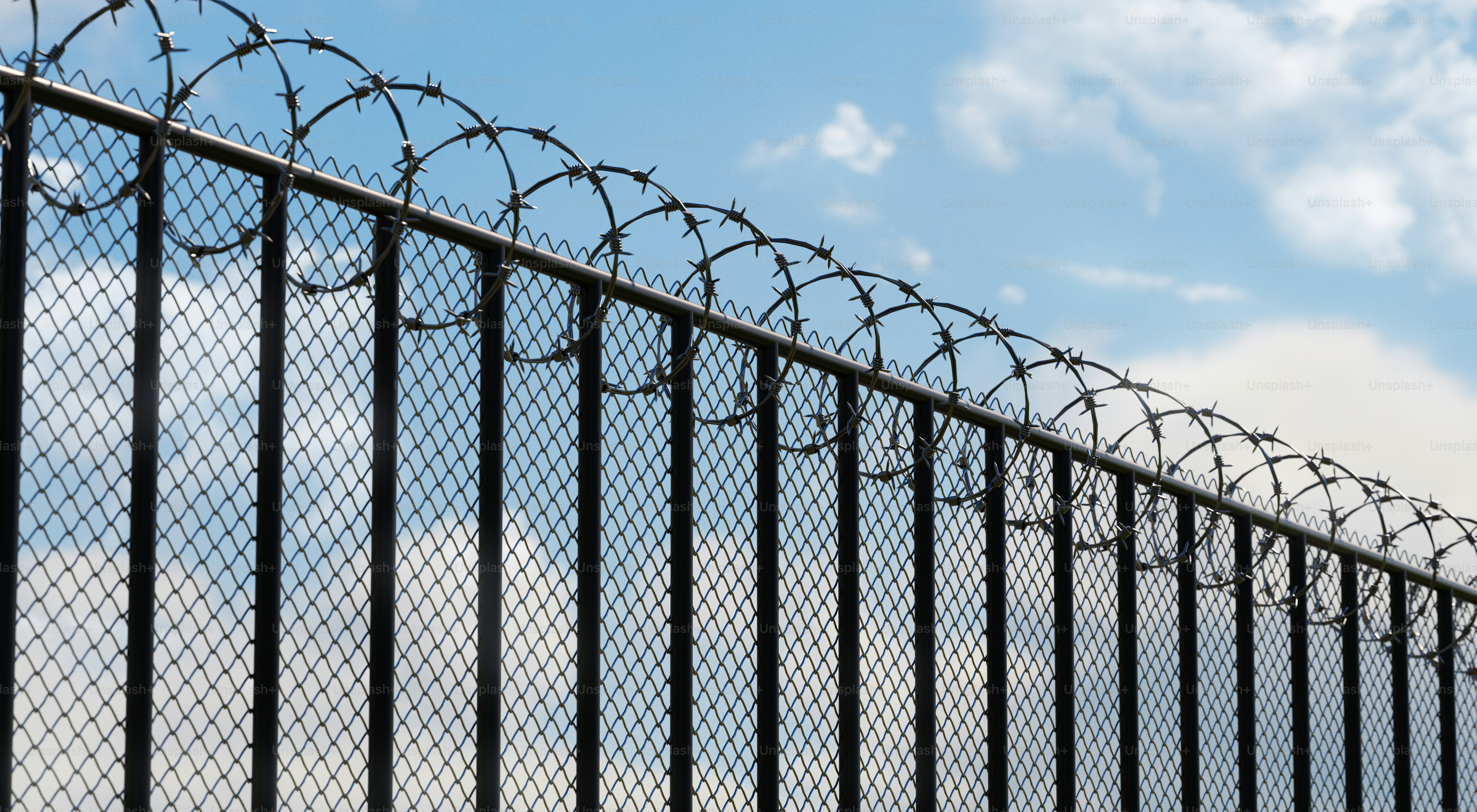 Recinzione di filo spinato contro un cielo azzurro nuvoloso