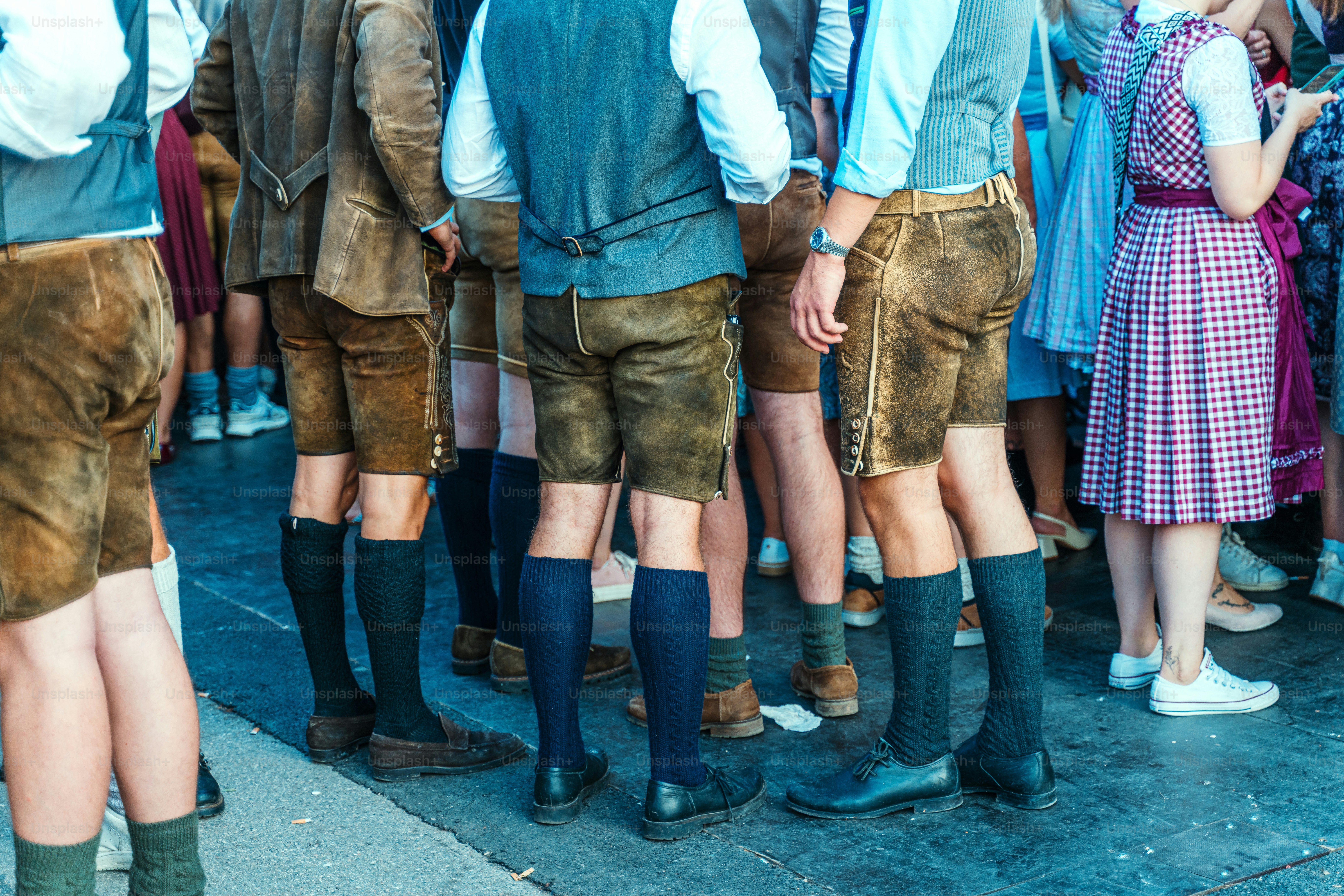 Crowd of friends and family in traditional Bavarian attire gather at Munich's Wiesn, the world's largest beer festival. Leather shorts, knee-high socks, and colorful dirndls create a lively, cultural scene.
