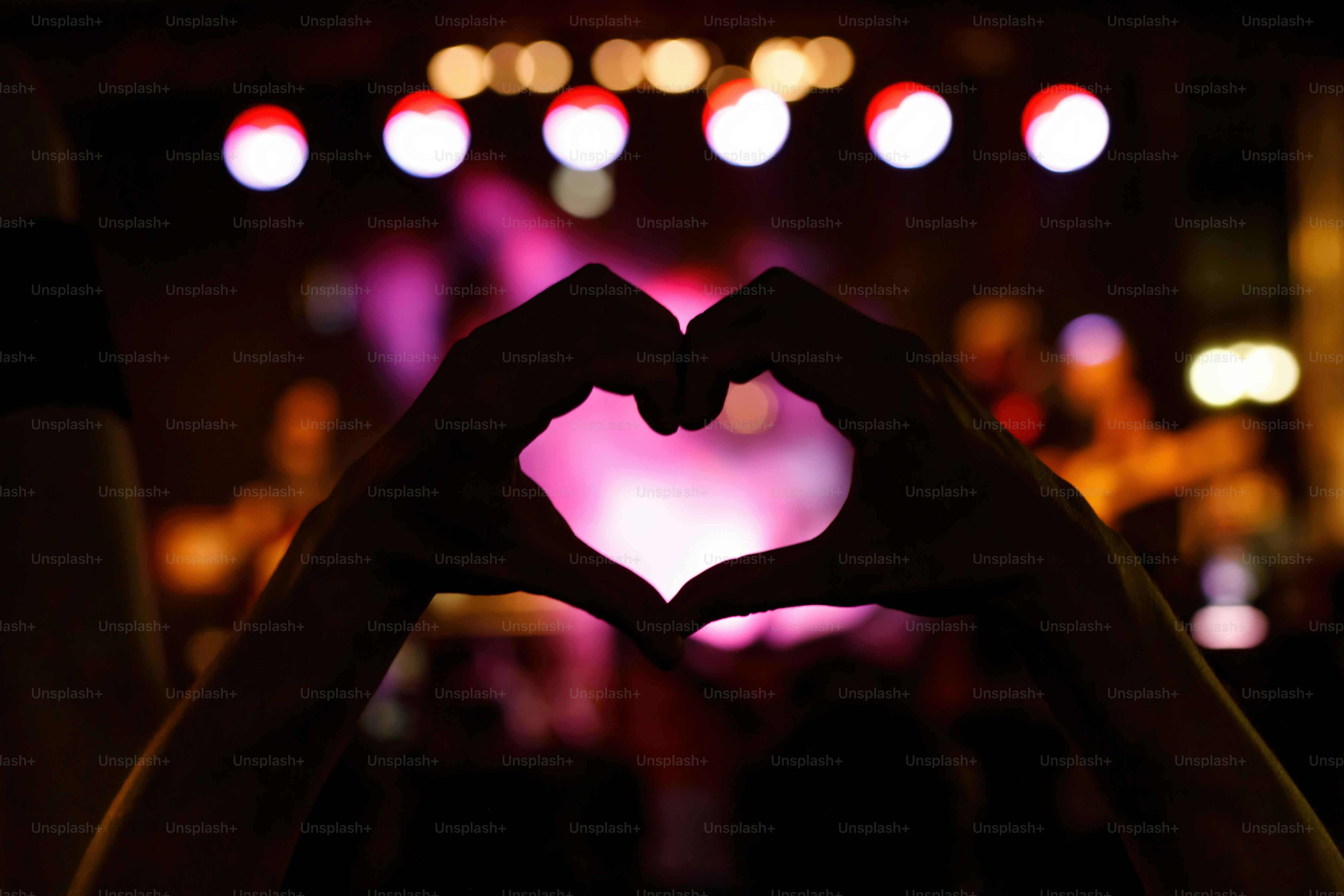 A person is making a heart sign during a concert of a favorite music band. Black silhouette