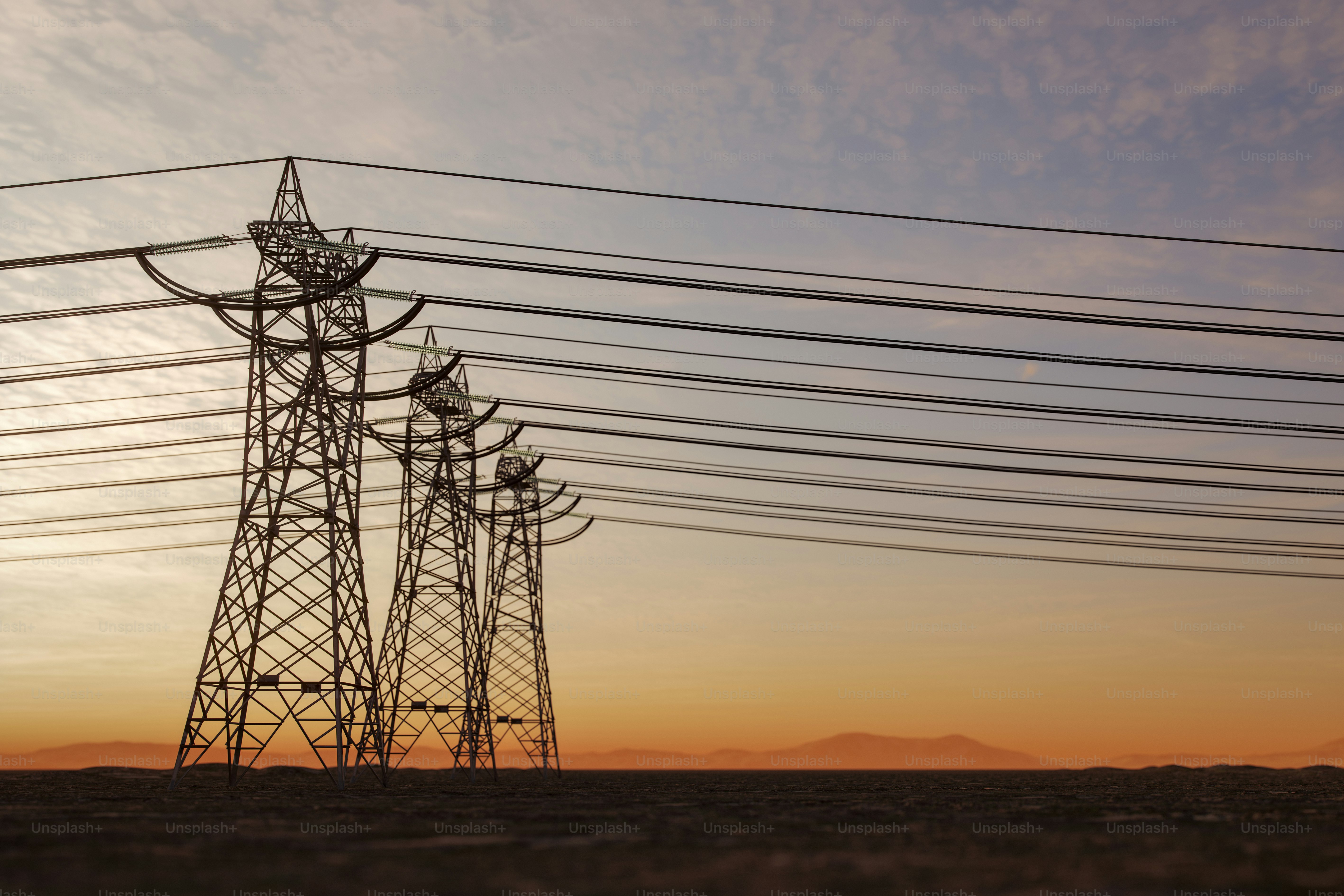 High voltage transmission towers silhouetted against a sunset sky.