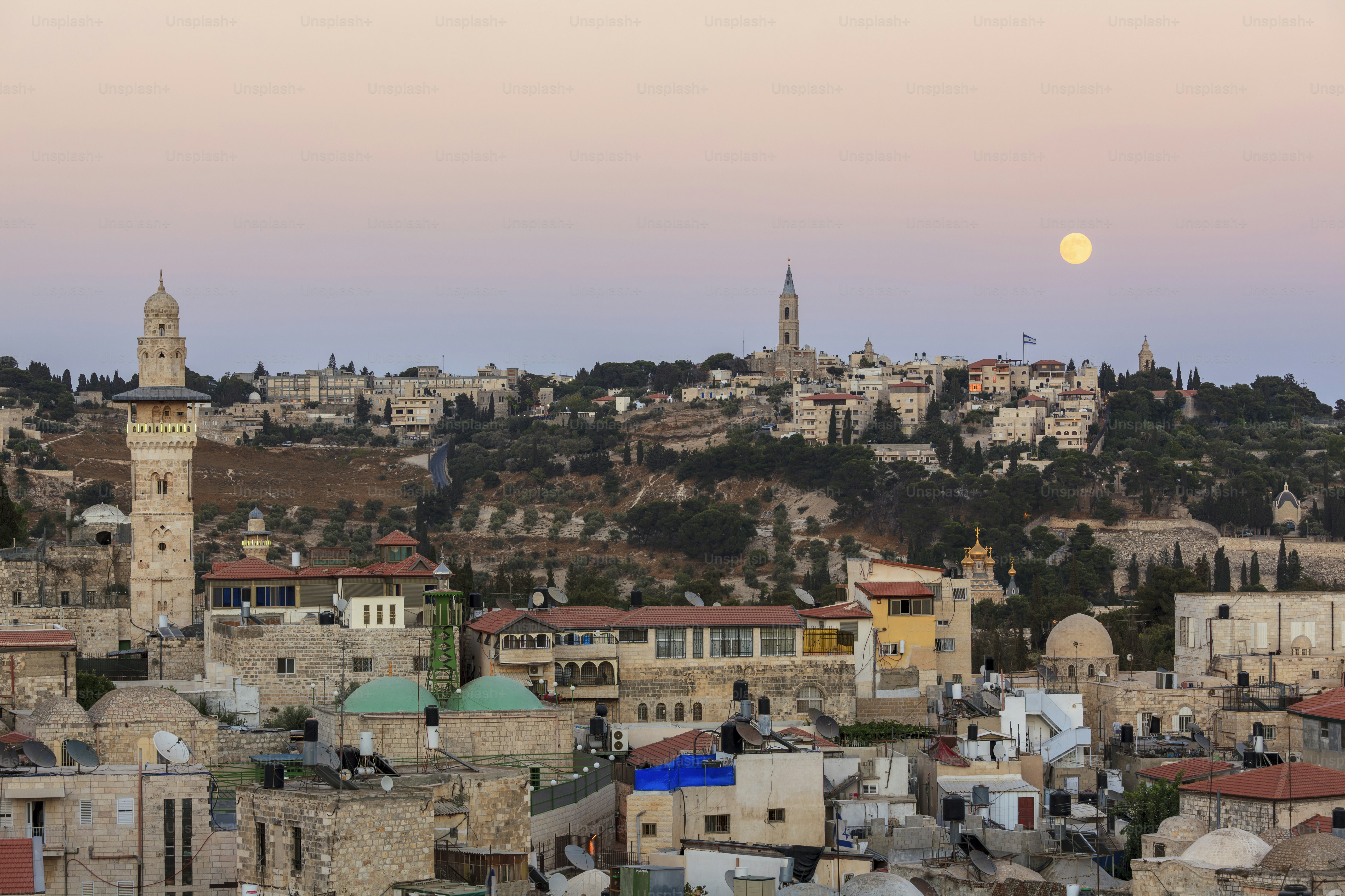 View of the Old City of Jerusalem with the Mount of Olives in the background and the moon rising above the horizon.
