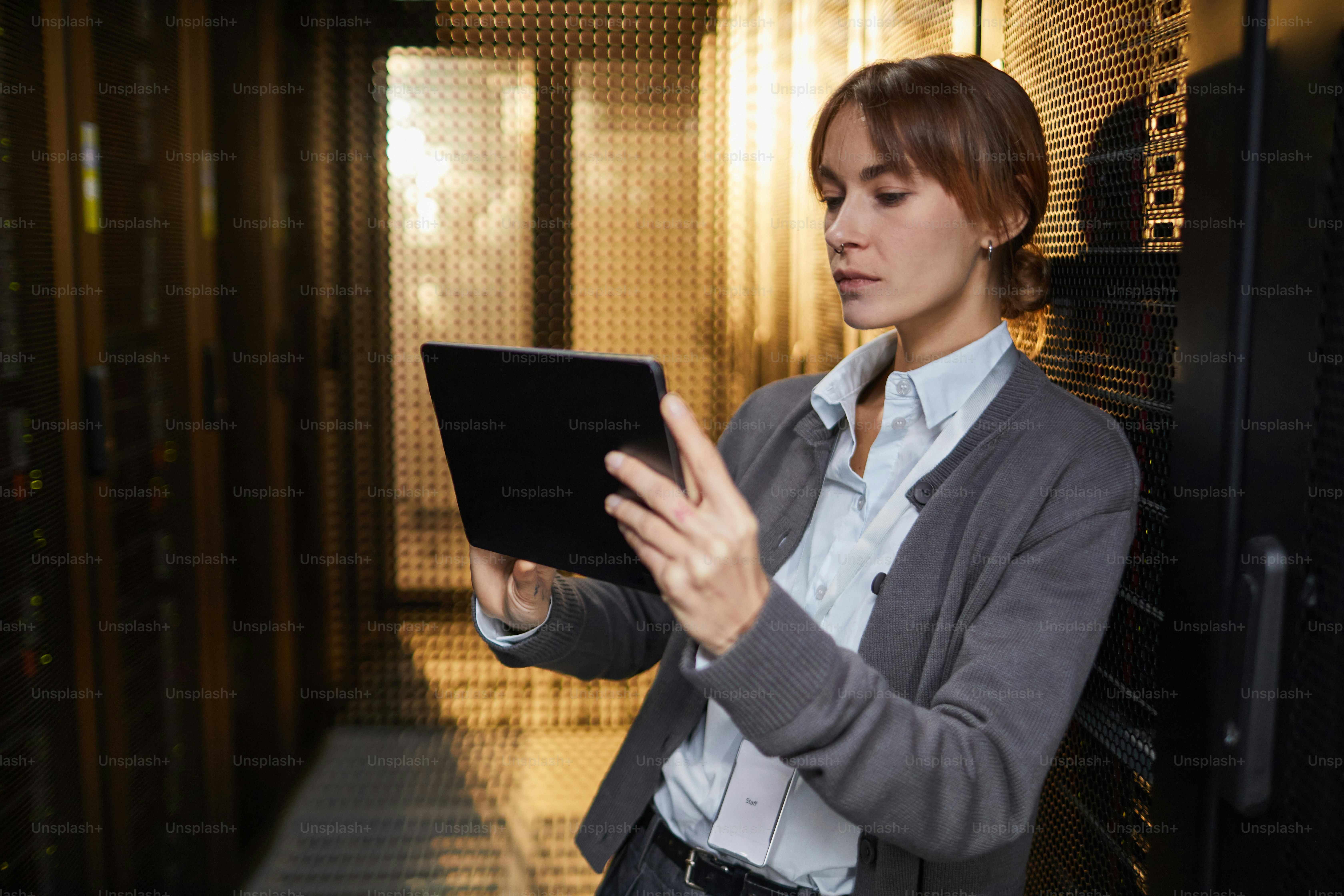 Caucasian IT professional examining data on tablet while standing in server room setting, surrounded by server racks and tech equipment