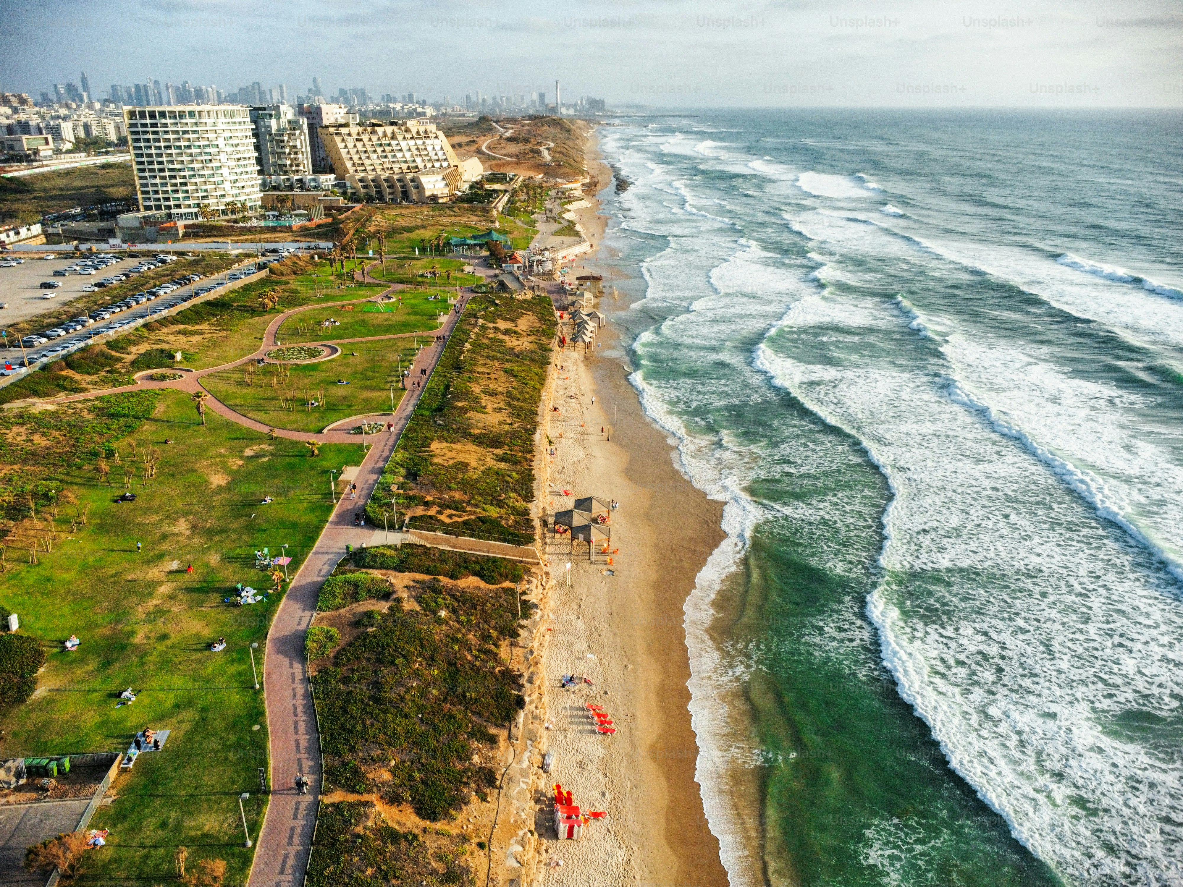 Aerial view of white water splashing on the beach in the right and city with buildings and factories and parks
