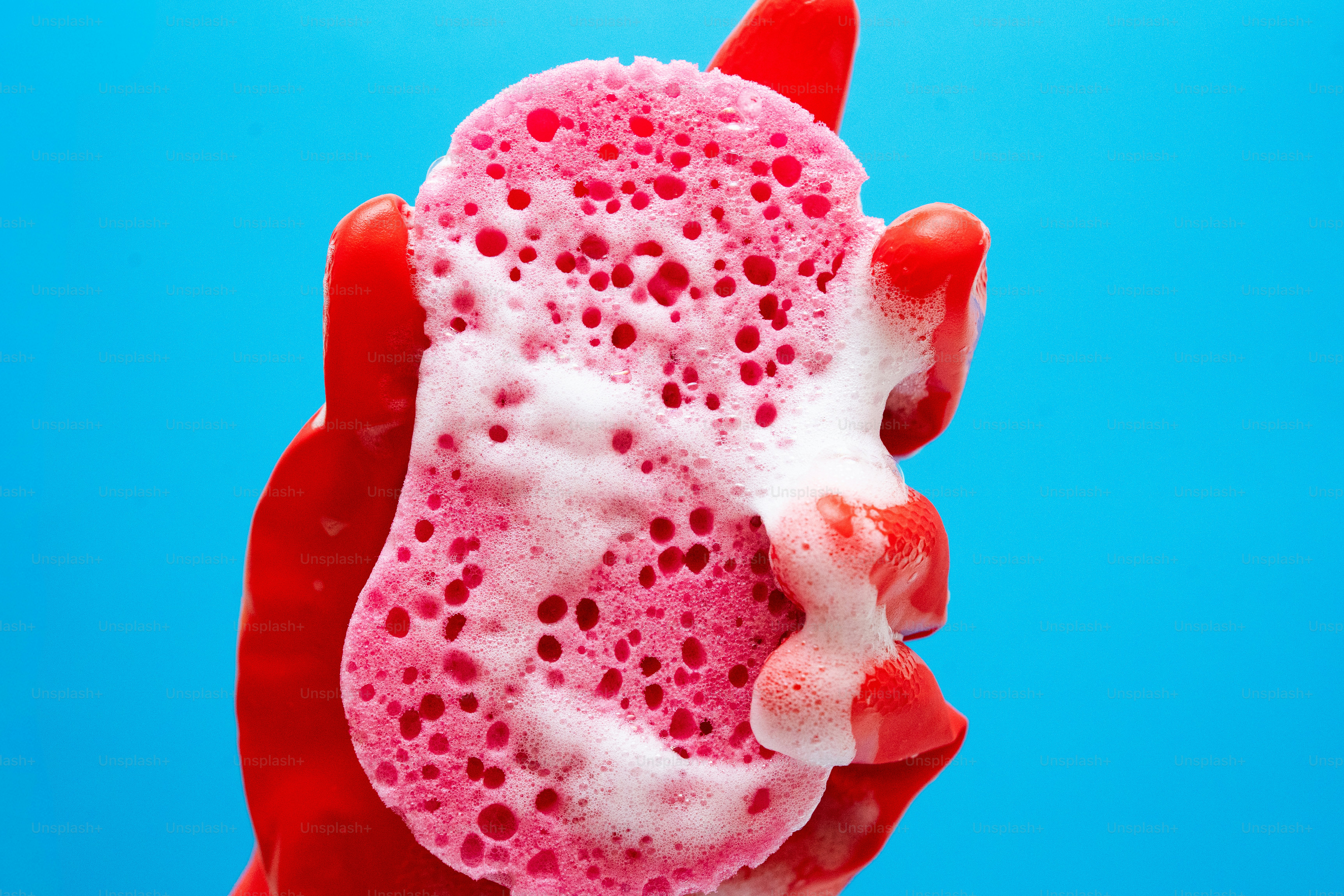 Red glove holding a pink sponge with soap bubbles