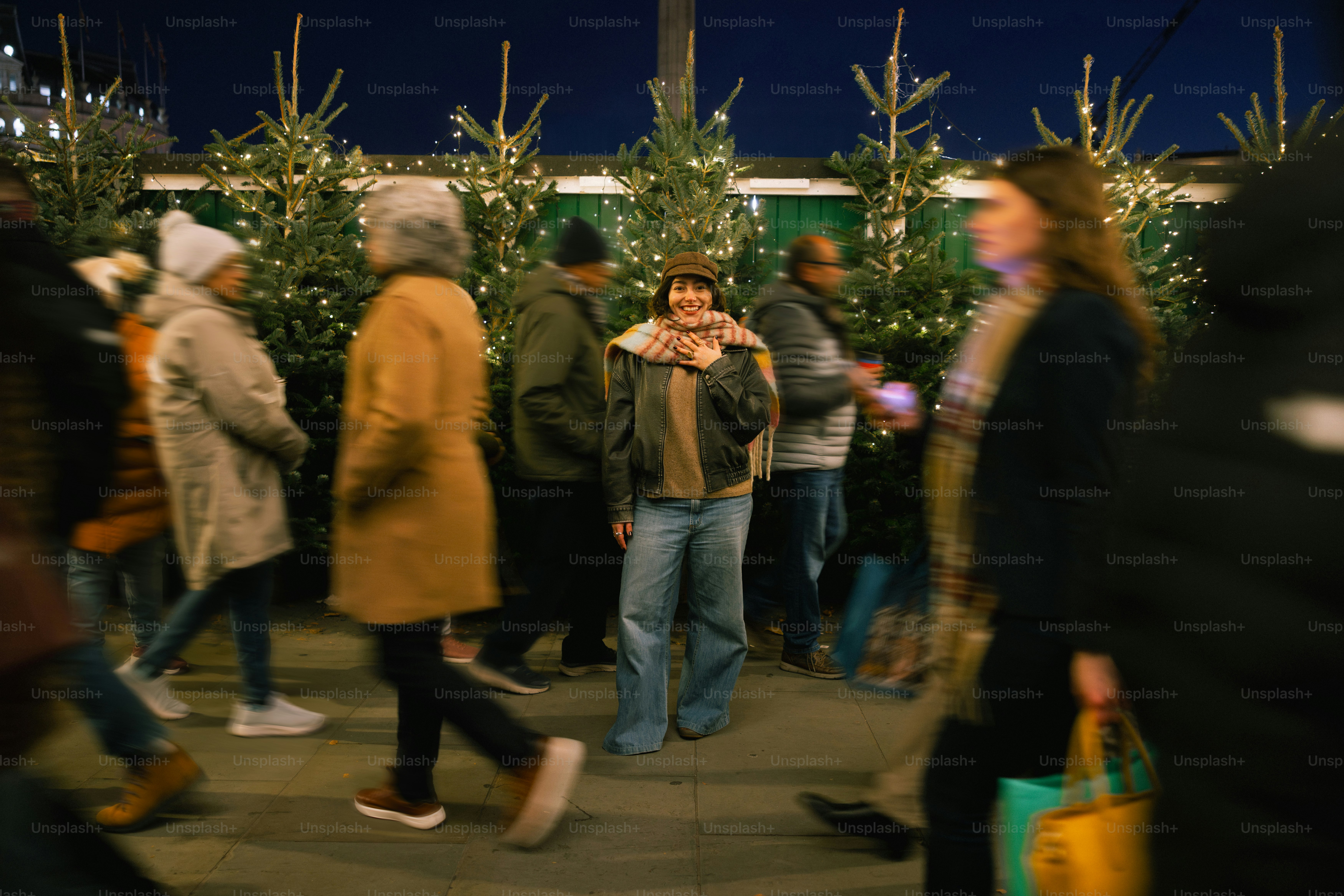 People walking past decorated christmas trees at night.