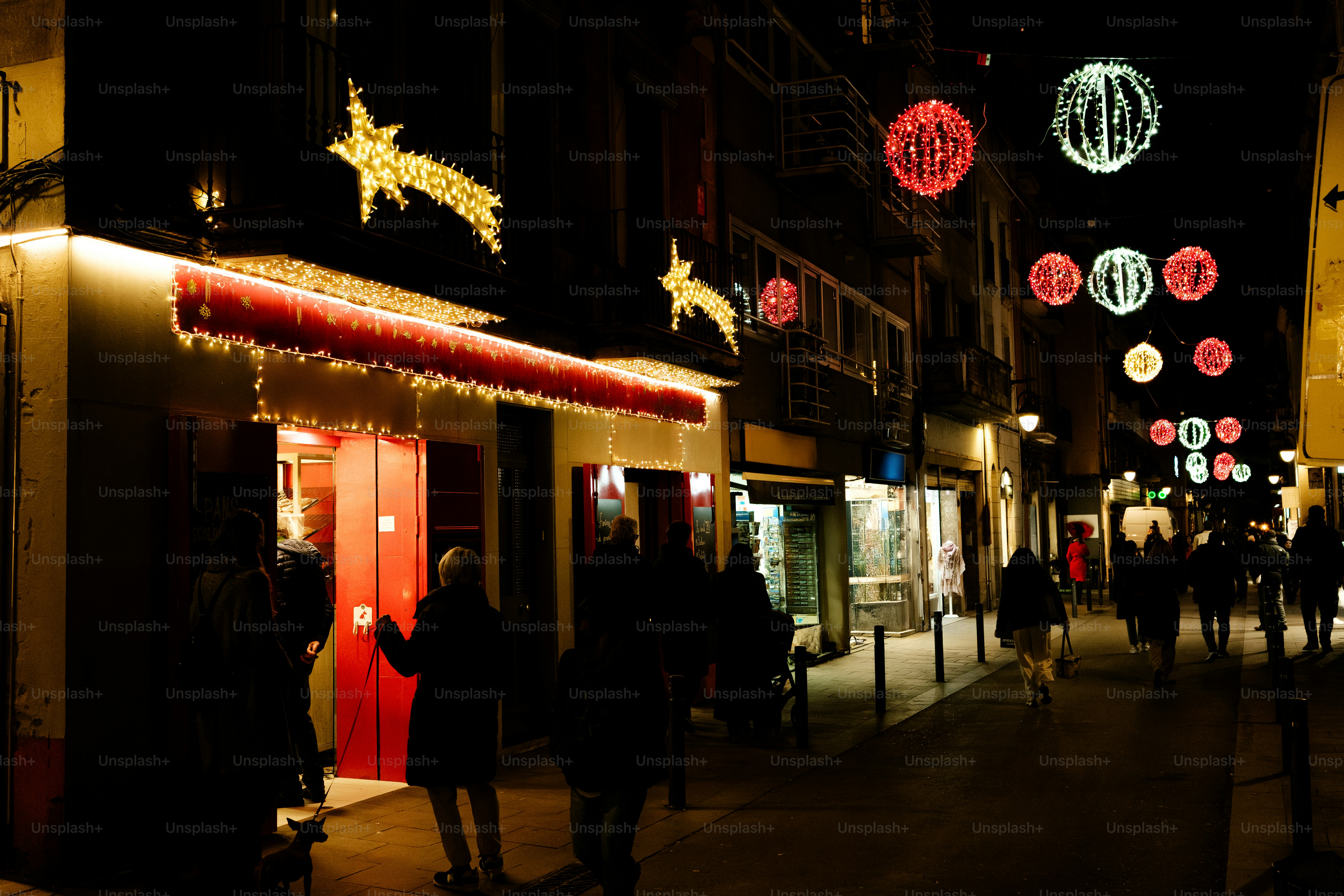 People walk down a street decorated with christmas lights.