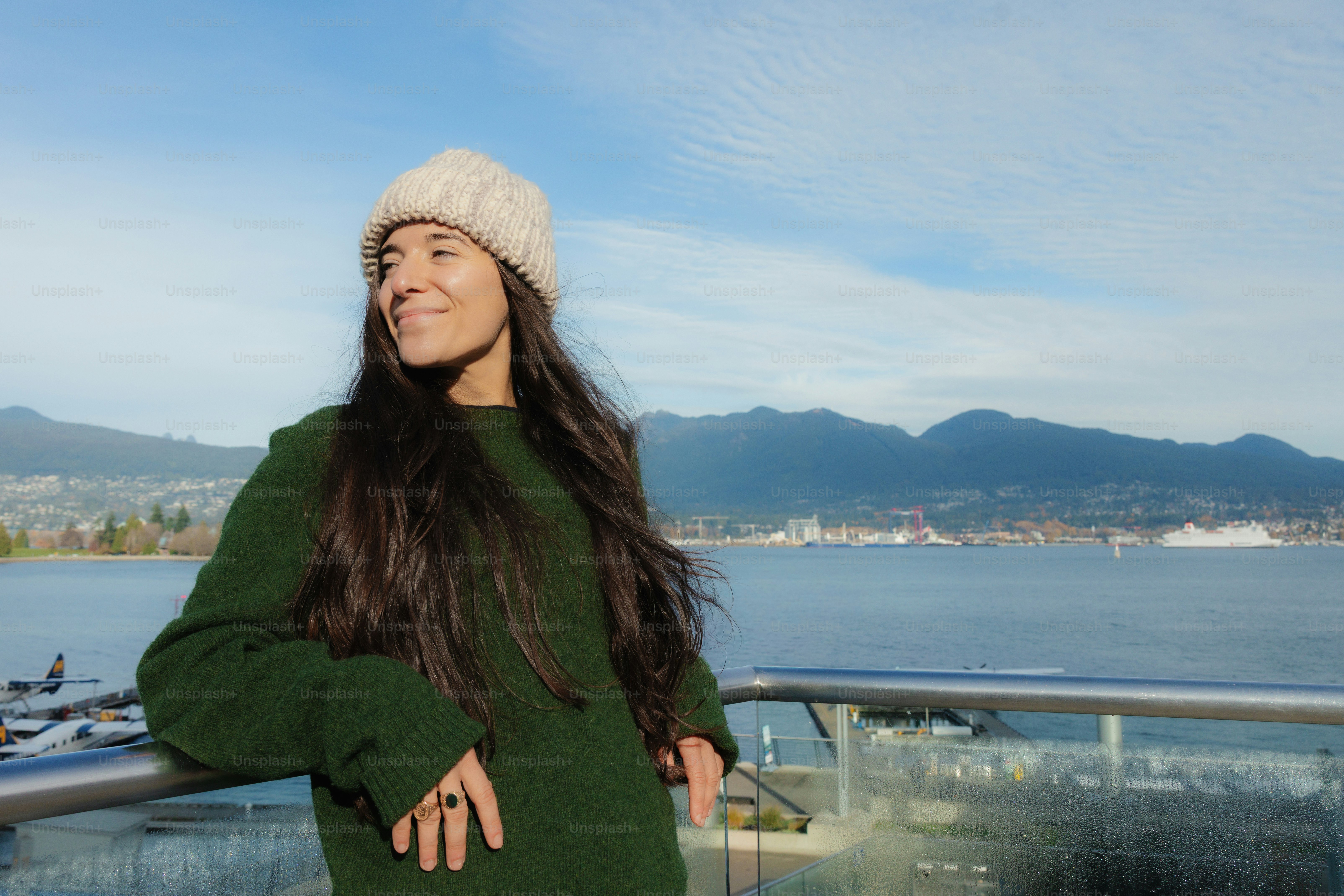 Woman in knit hat and green sweater by the water.