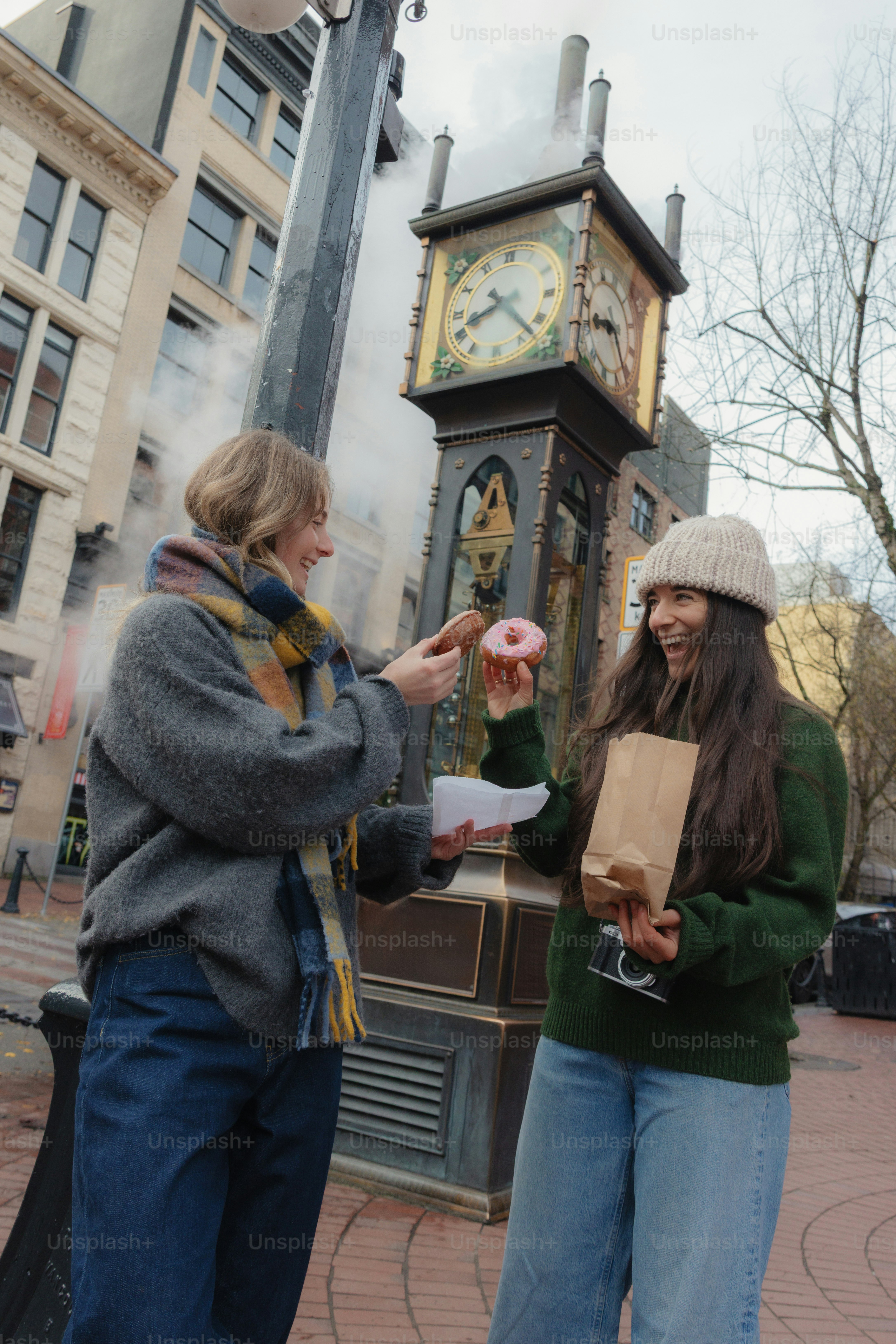 Two women sharing donuts near a clock tower