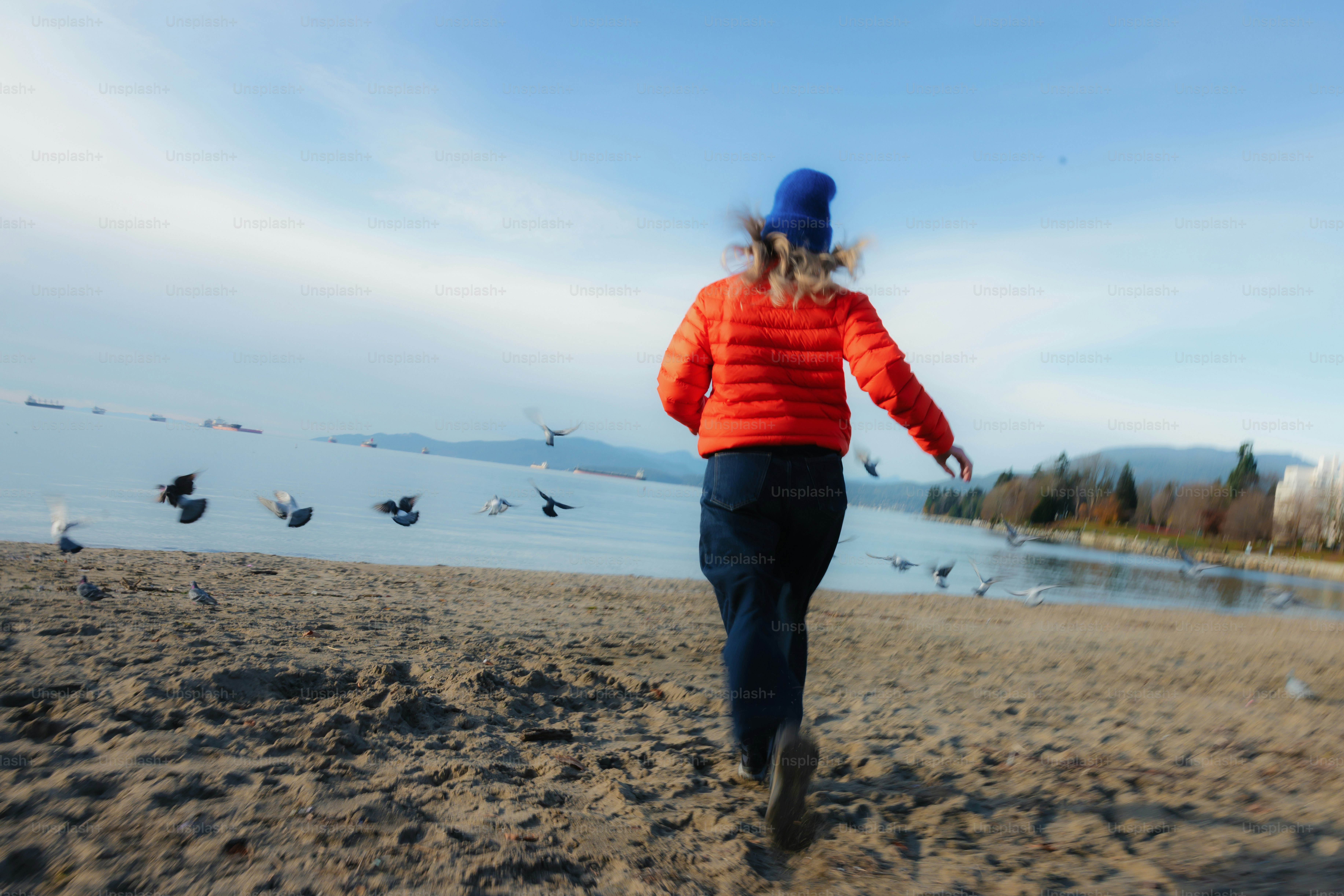 Woman running on beach towards lake with birds flying