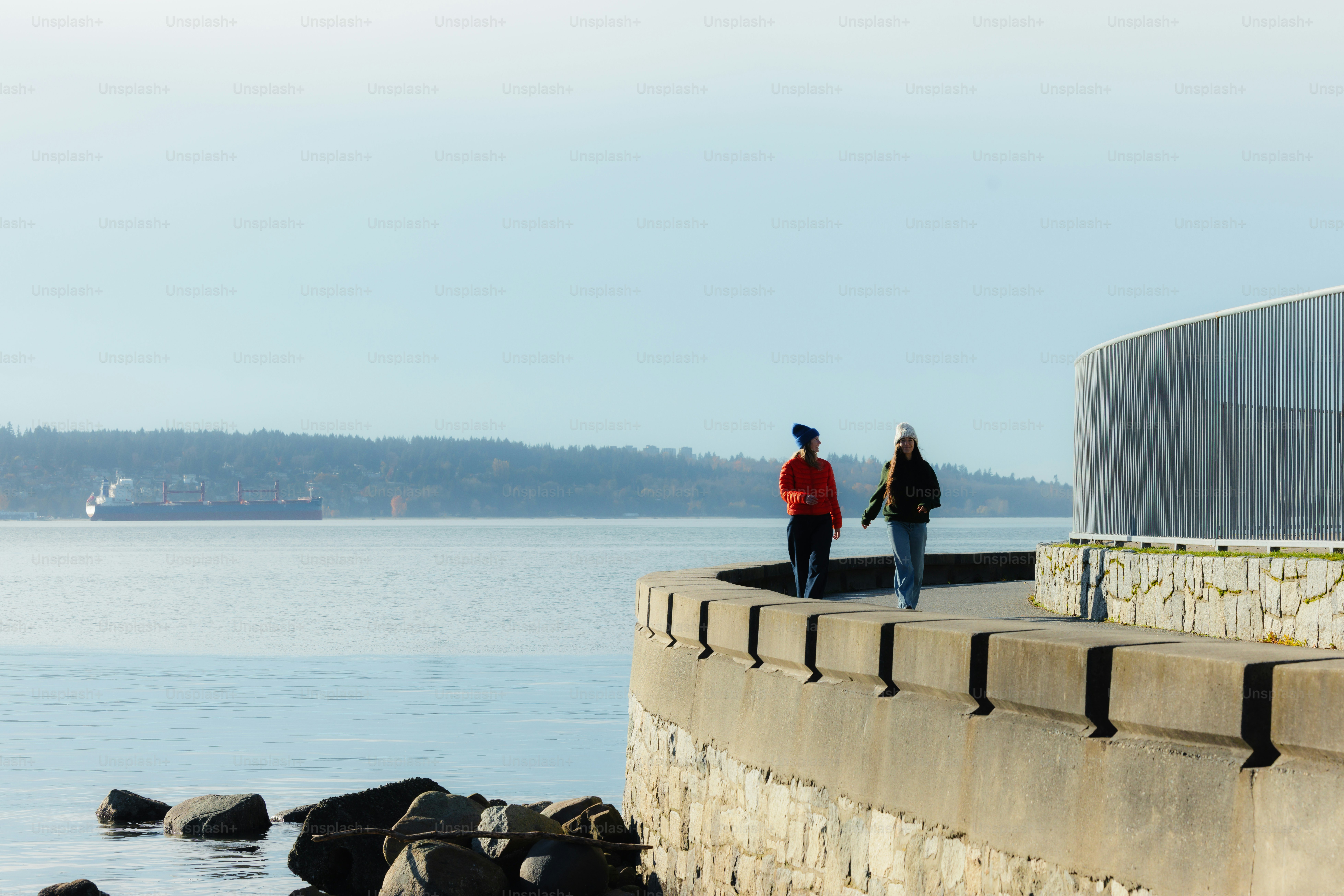 Two people walk along a waterfront promenade.