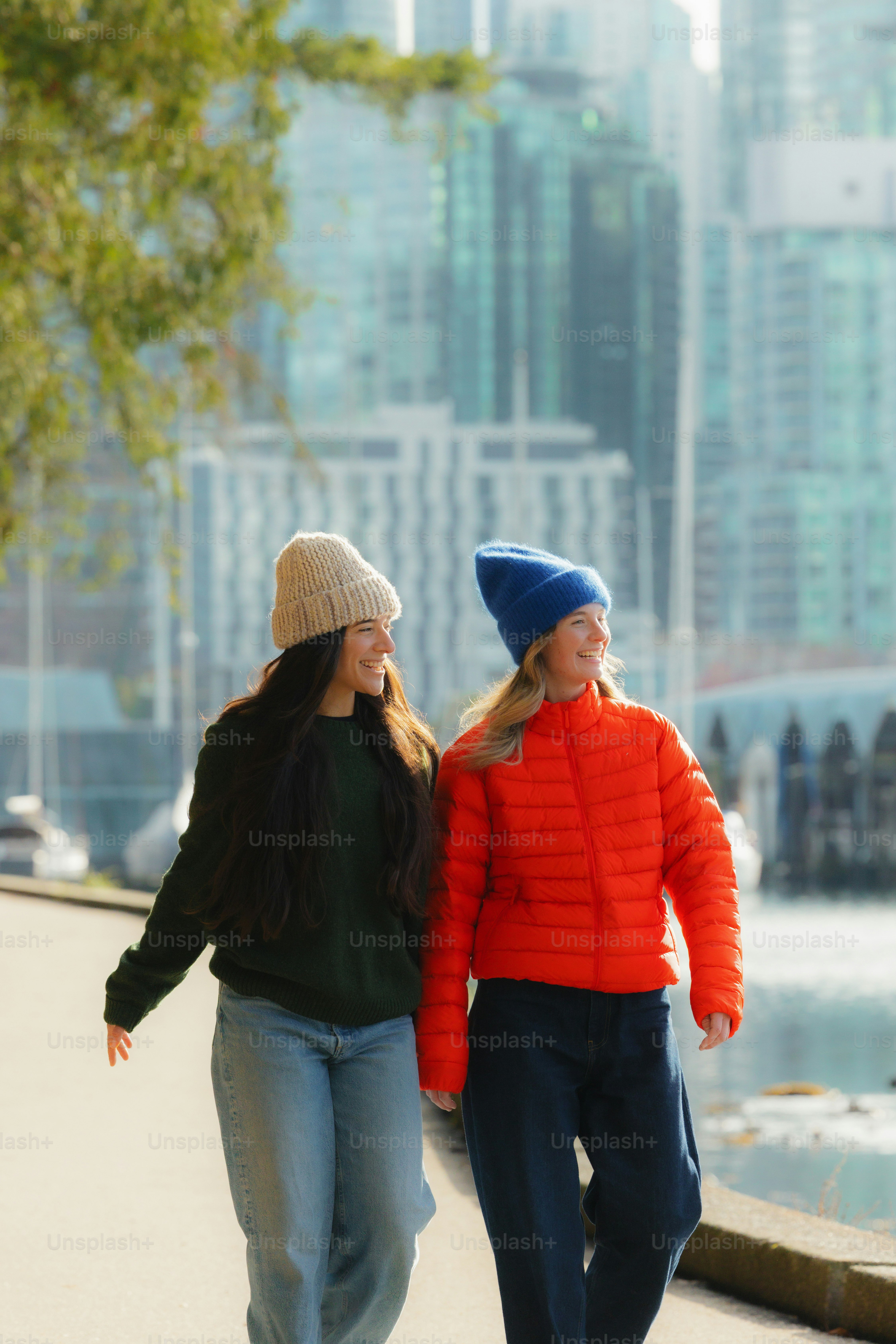Two women walking outdoors near water and buildings