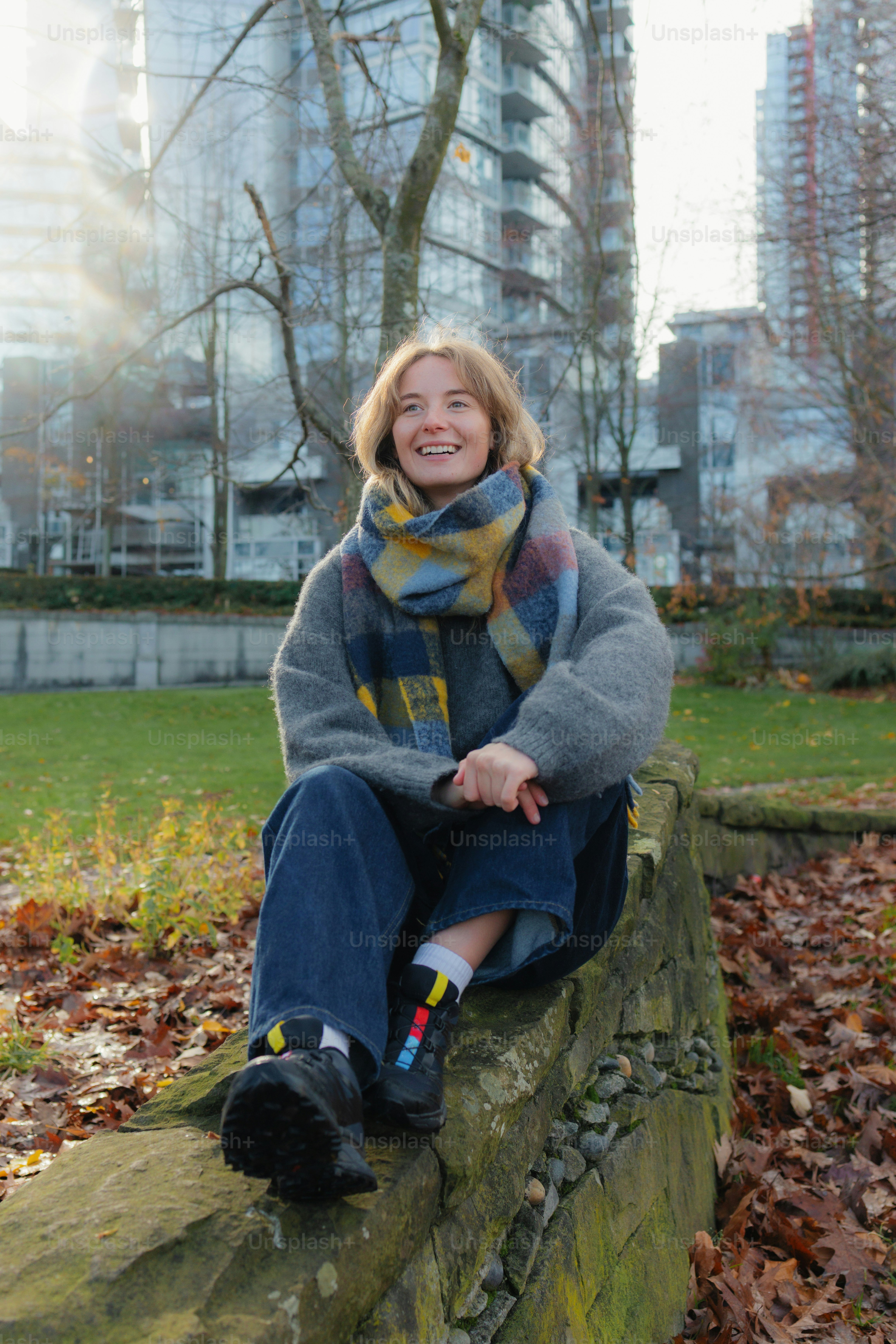 A woman sitting on a stone wall in a park.