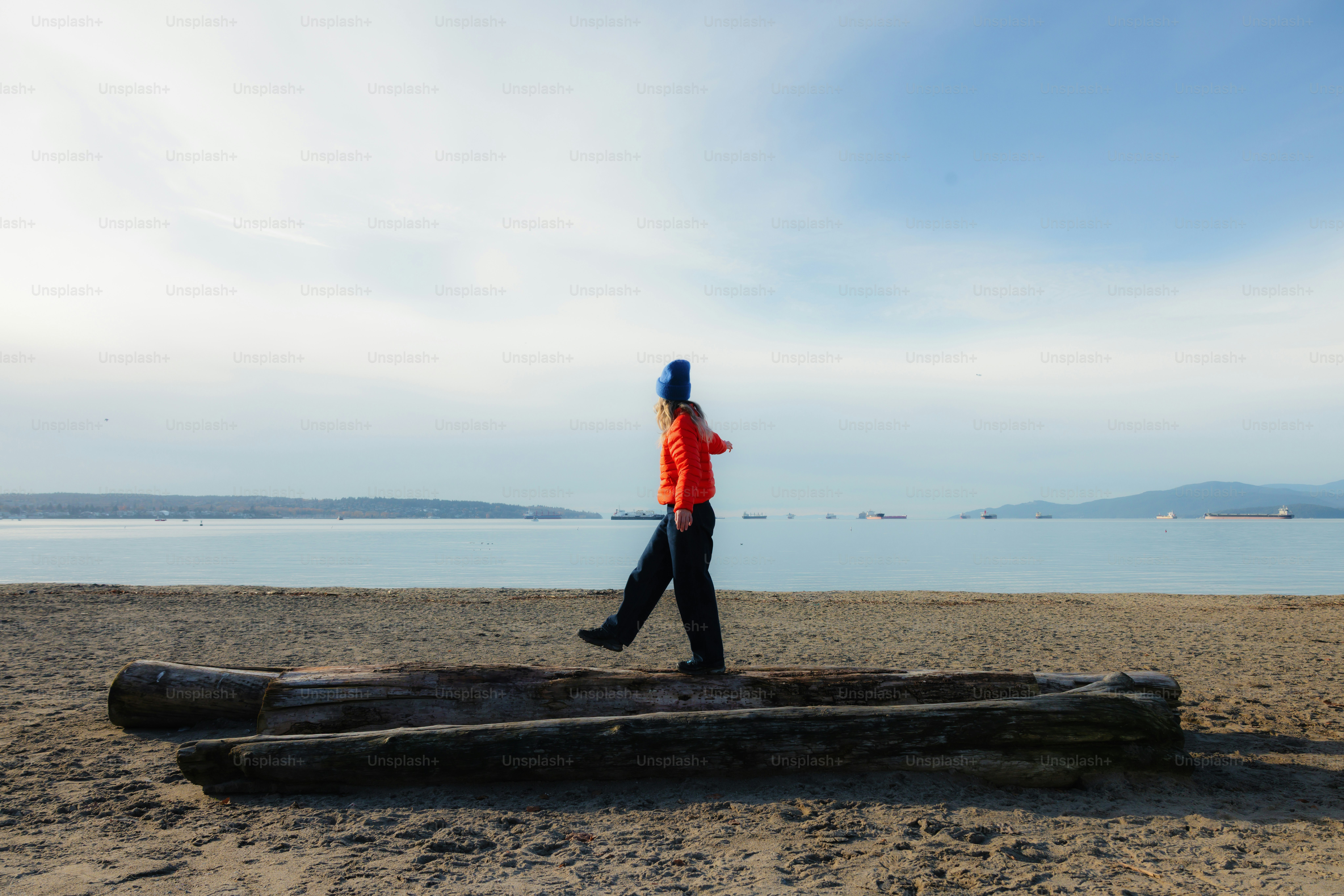 Person walks on driftwood log at beach