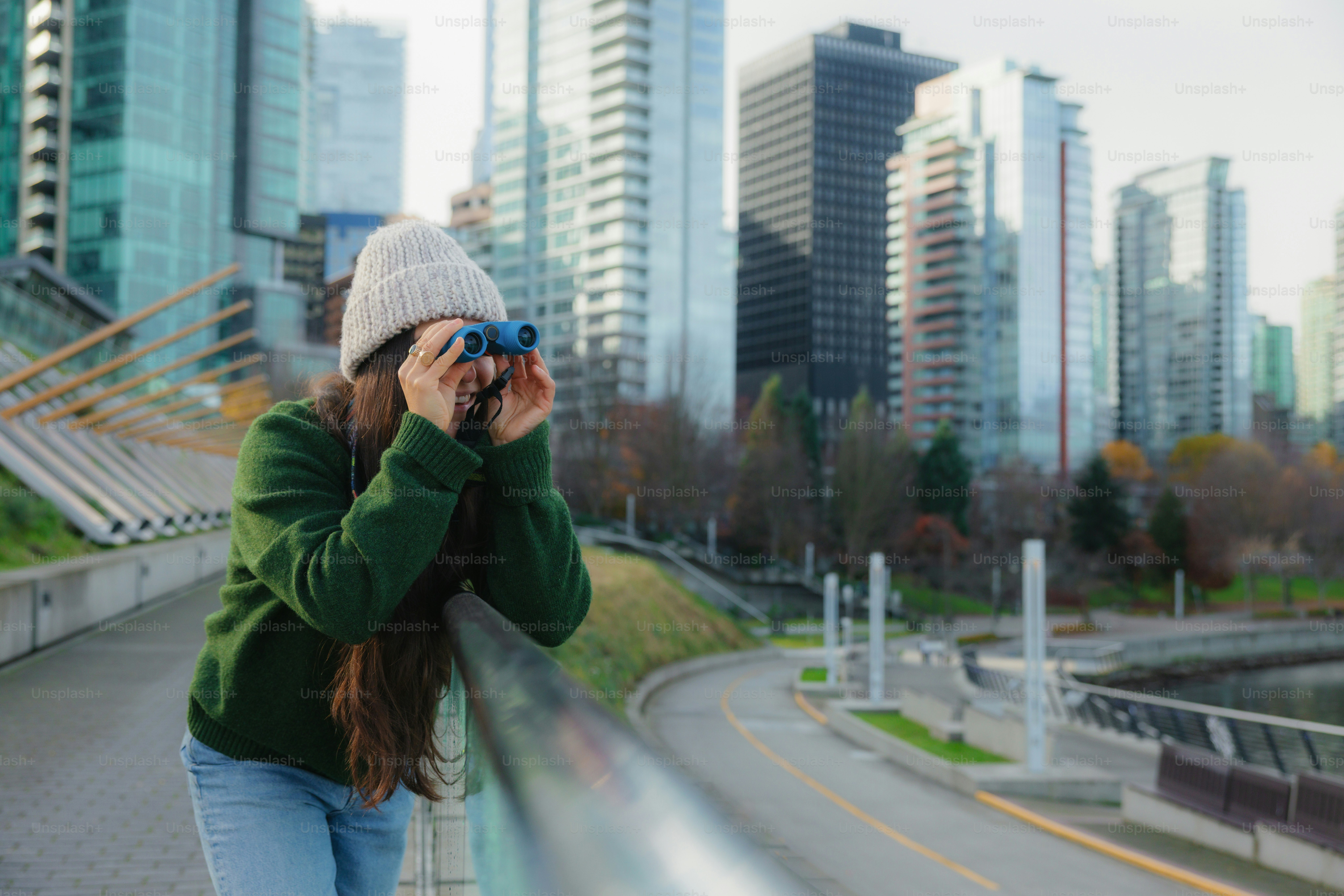 Mujer mirando por prismáticos con edificios de la ciudad detrás.
